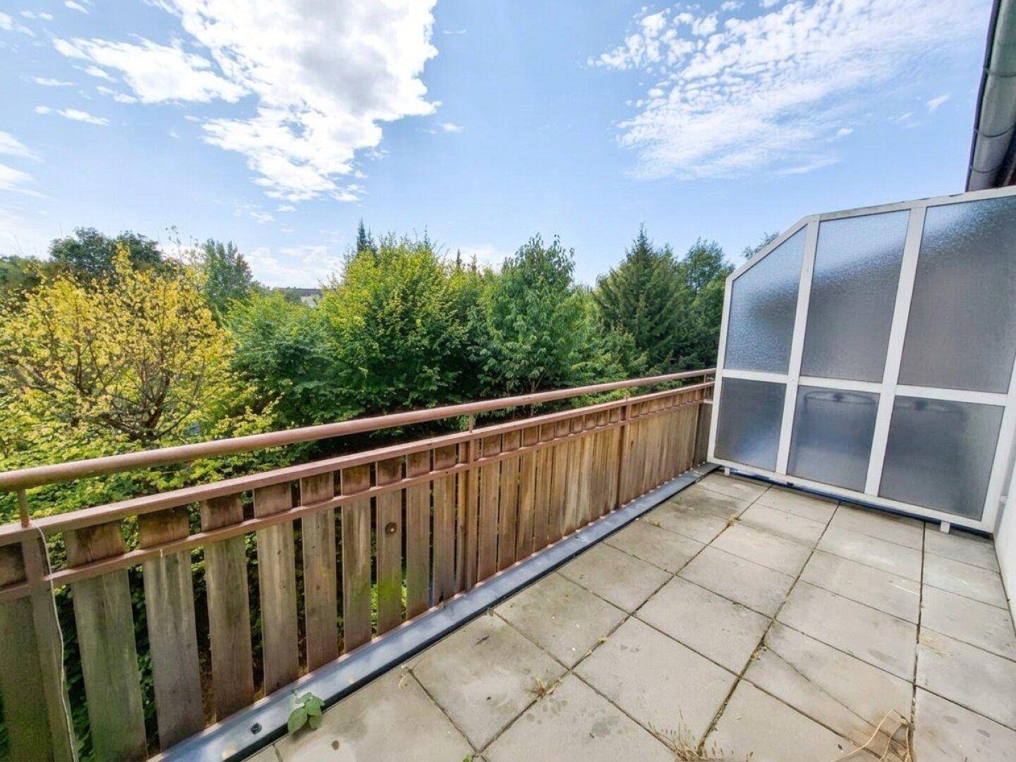 Geräumiger Balkon mit Fliesenboden, Holzgeländer und Blick ins Grüne.