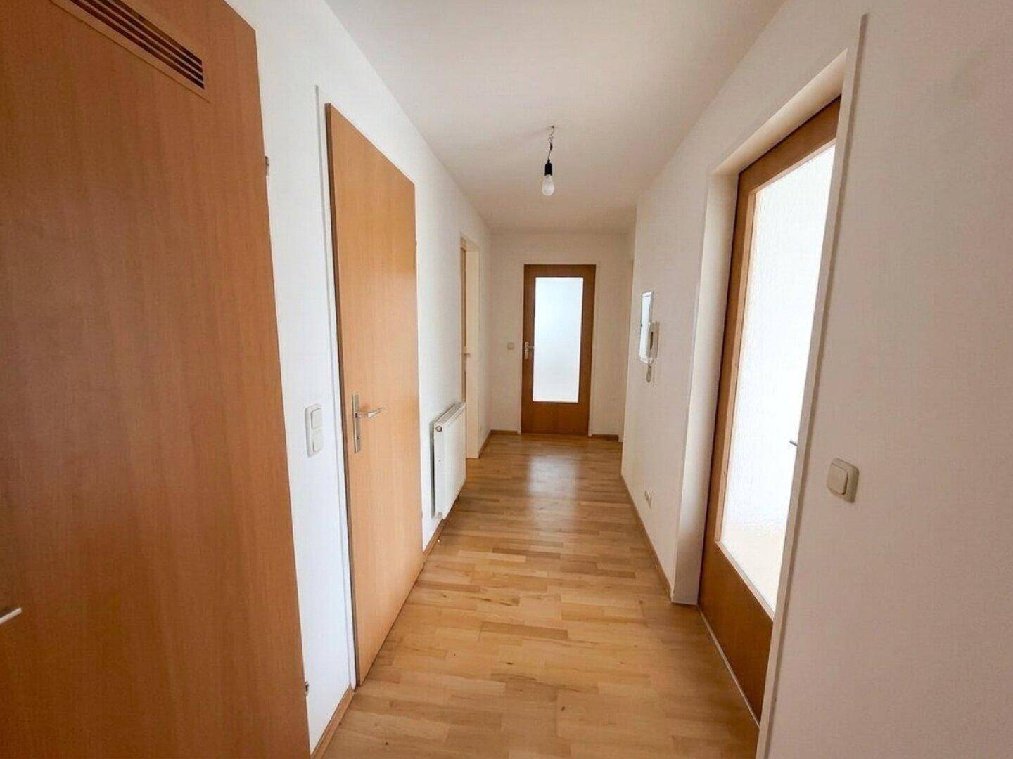 Heller Flur mit Holztüren, Parkettboden und weißen Wänden, der zu weiteren Räumen führt.