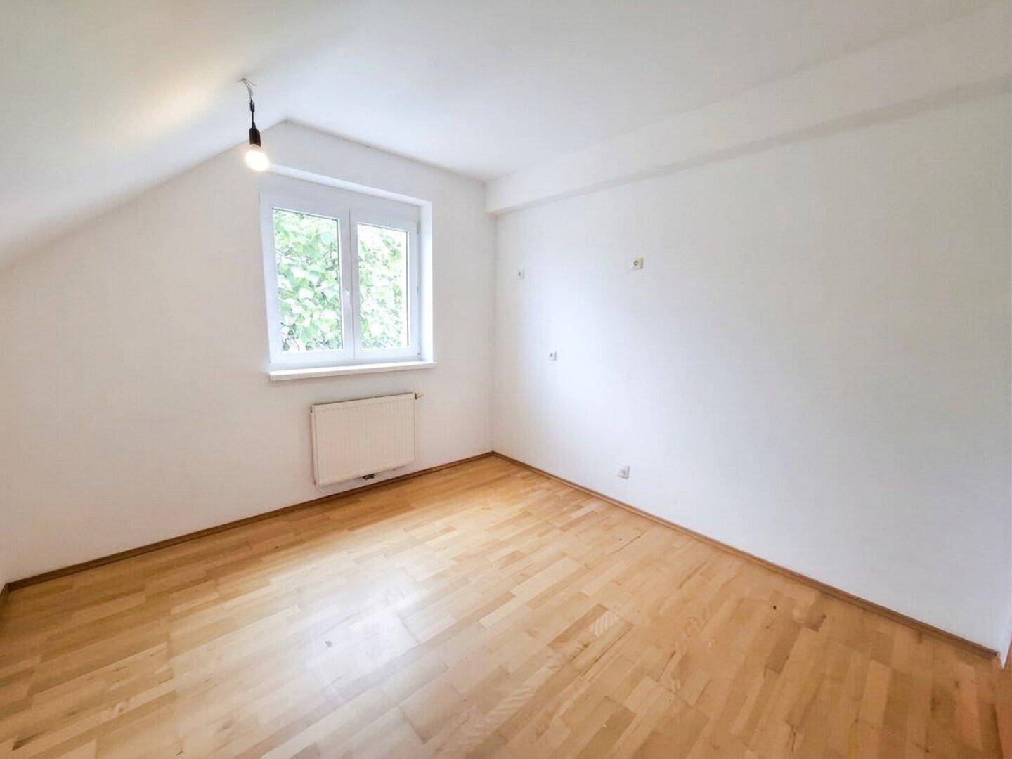 Dachzimmer mit Parkettboden, weißen Wänden und einem Fenster für natürliches Licht.