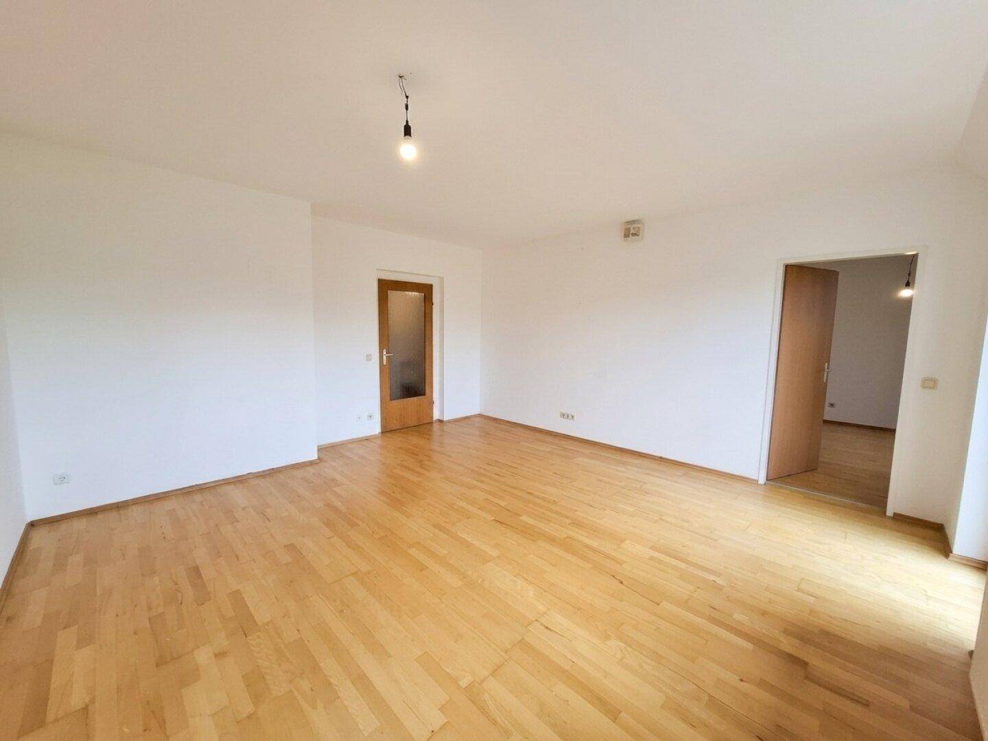 Geräumiges Zimmer mit hellem Parkettboden und zwei Holztüren.