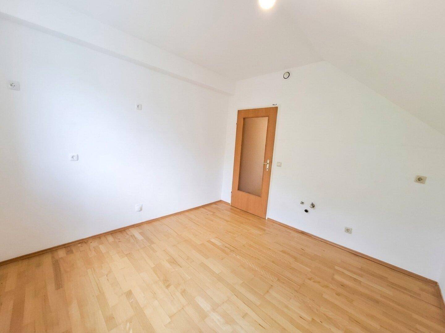 Geräumiges Dachzimmer mit Parkettboden, schrägen Wänden und einer Holztür.