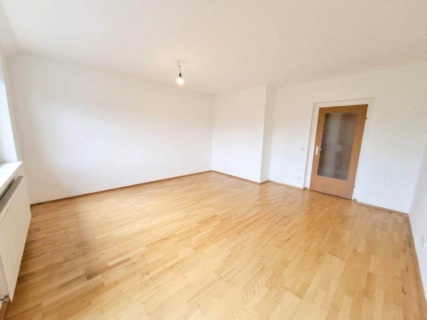 Heller Raum mit Parkettboden, weiß gestrichenen Wänden und einer Holztür.