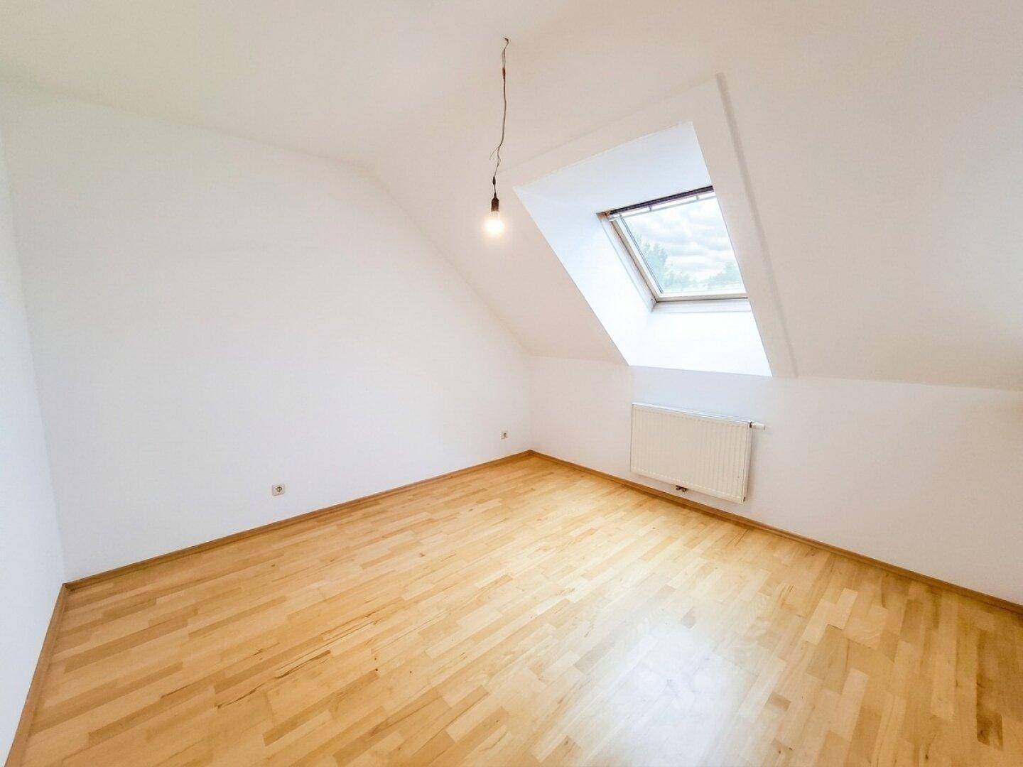 Dachzimmer mit Parkettboden, schrägen Wänden und einem großen Dachfenster.