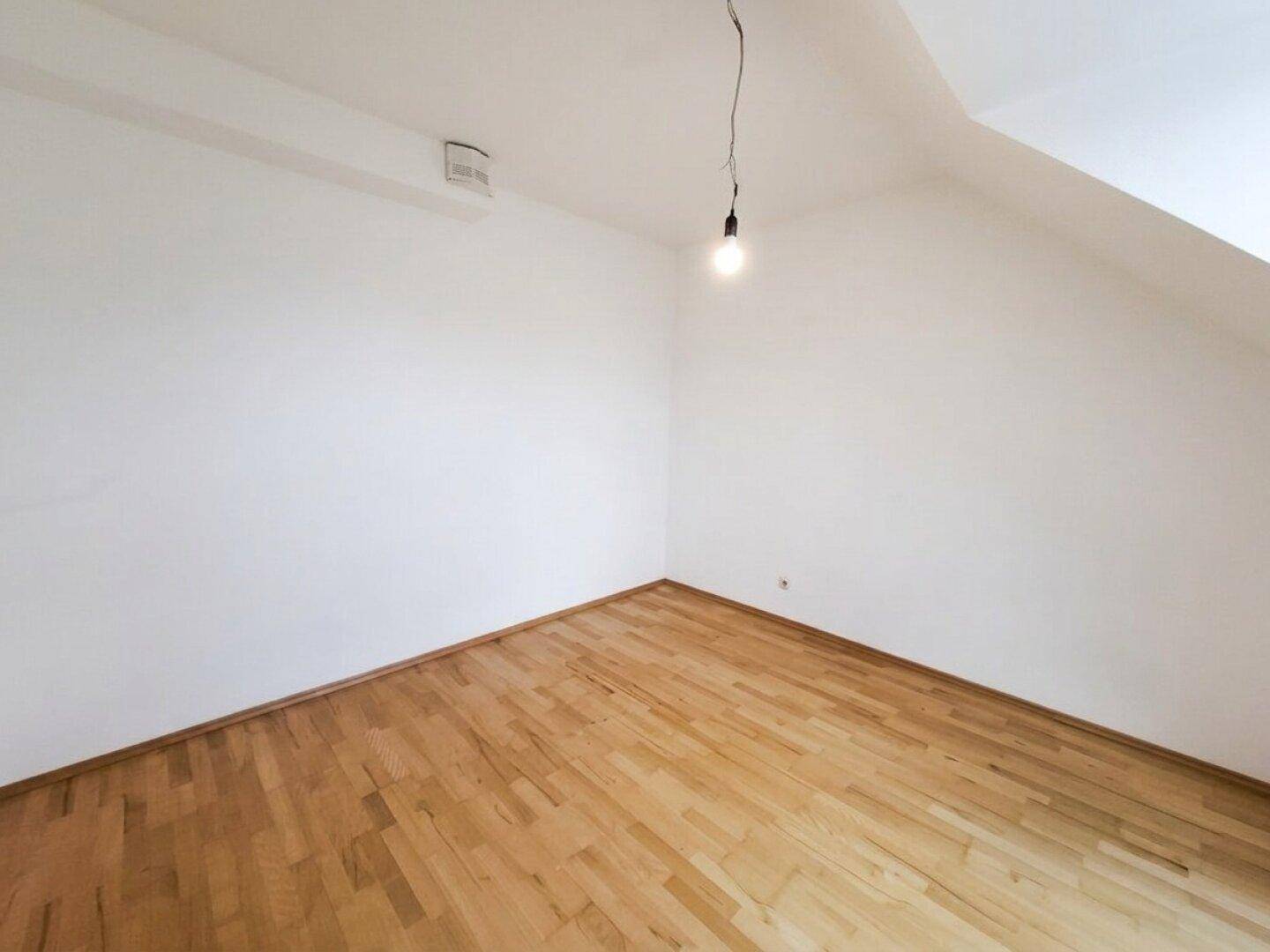 Geräumiges Dachzimmer mit Parkettboden und schrägen Wänden.