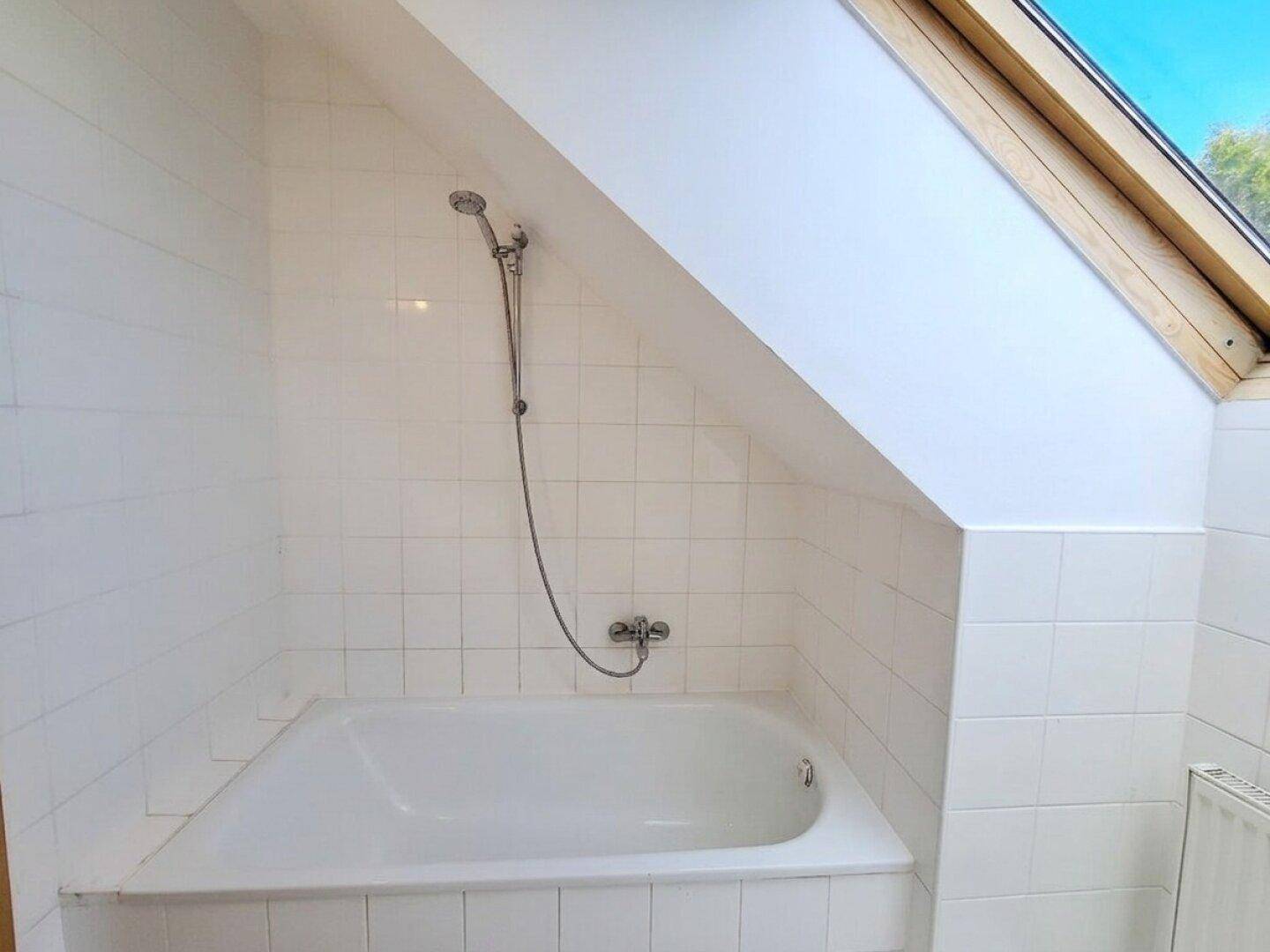 Gefliestes Badezimmer im Dachgeschoss mit Badewanne und Duscharmatur.