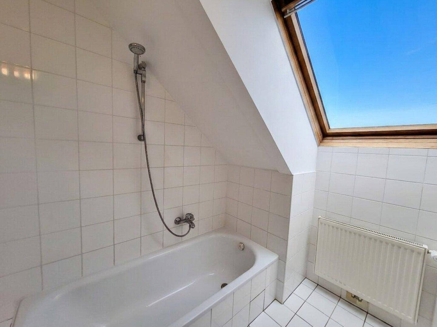 Badezimmer im Dachgeschoss mit Badewanne, Duscharmatur und Dachfenster.
