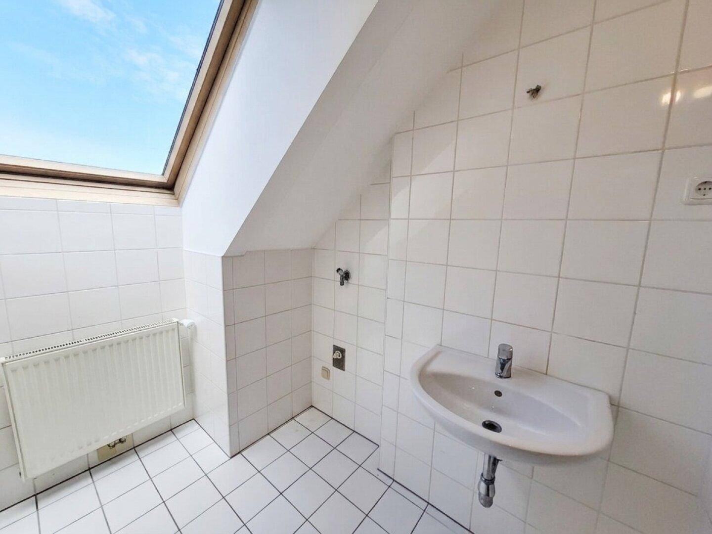 Gefliestes Badezimmer im Dachgeschoss mit Waschbecken, Heizkörper und Dachfenster.