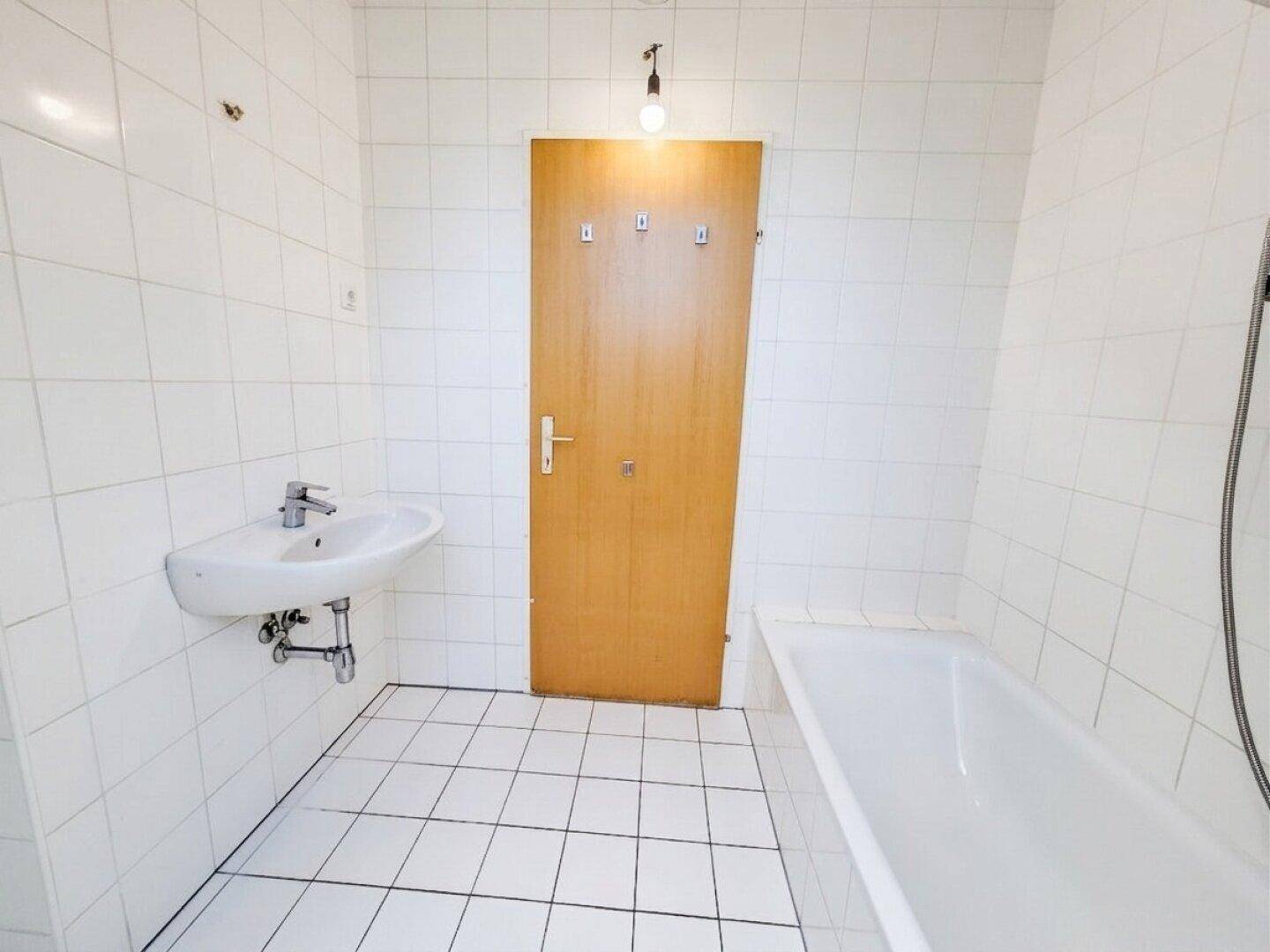 Badezimmer im Dachgeschoss mit Waschbecken, Badewanne und Holztür.