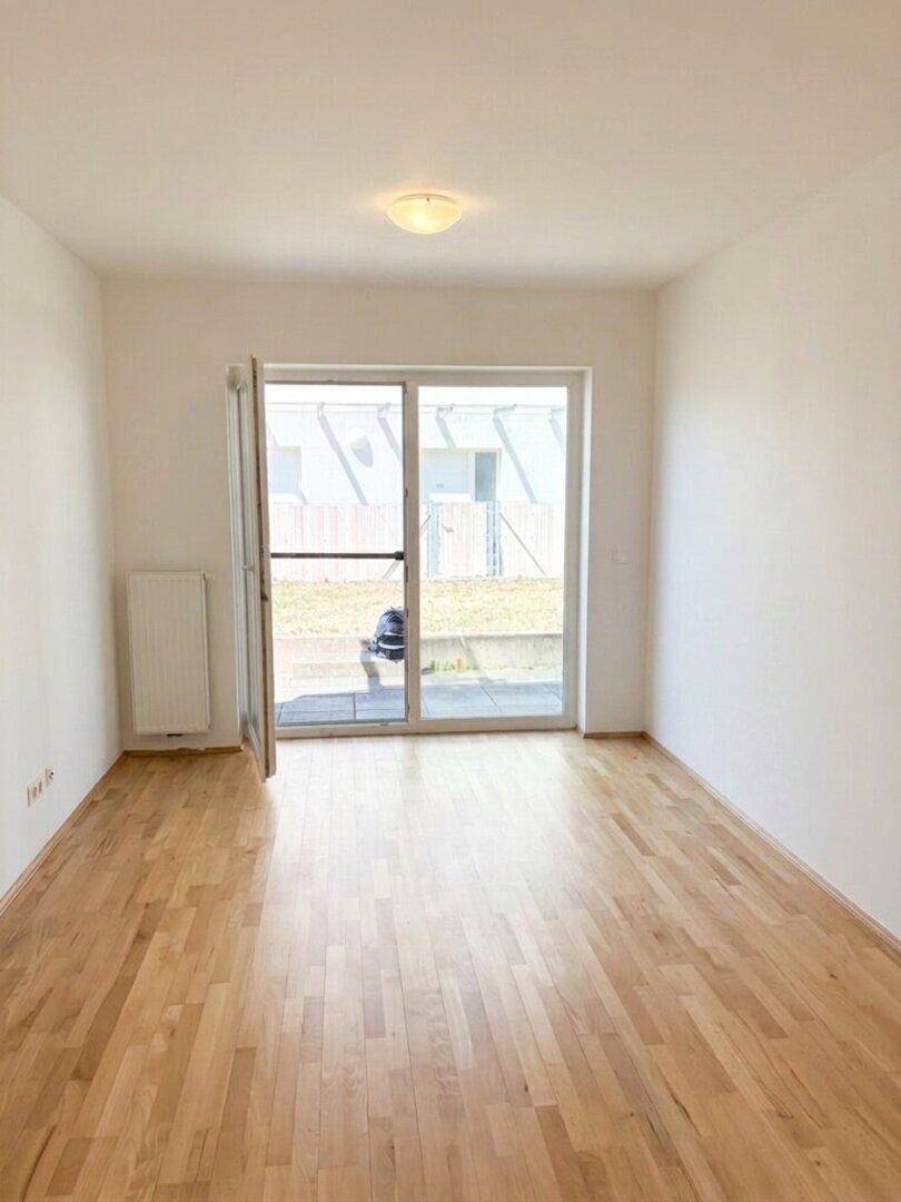 Heller Raum mit Parkettboden und großer Schiebetür, die ins Freie führt.