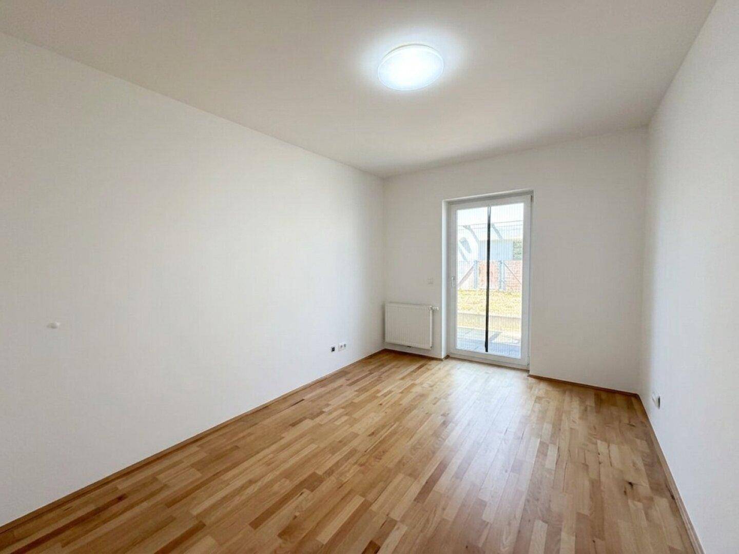 Leeres Schlafzimmer mit Parkettboden und viel Tageslicht durch die Terrassentür.