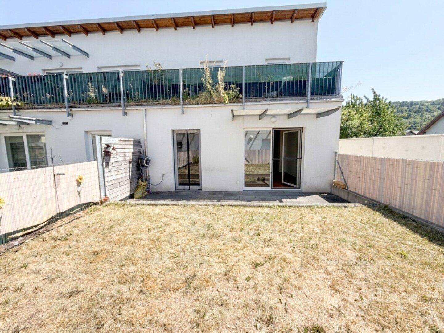 Gartenbereich mit Zugang zum Gebäude und einem Balkon im Obergeschoss.