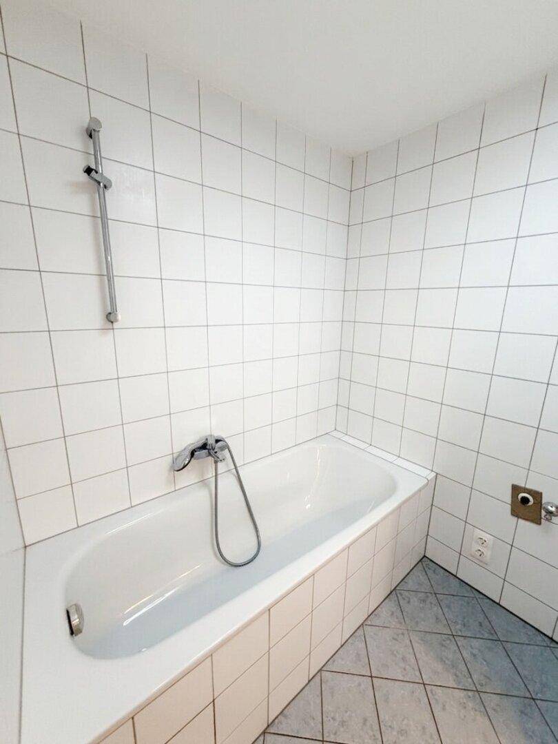 Detailansicht der Badewanne mit Duscharmatur und weißen Wandfliesen.