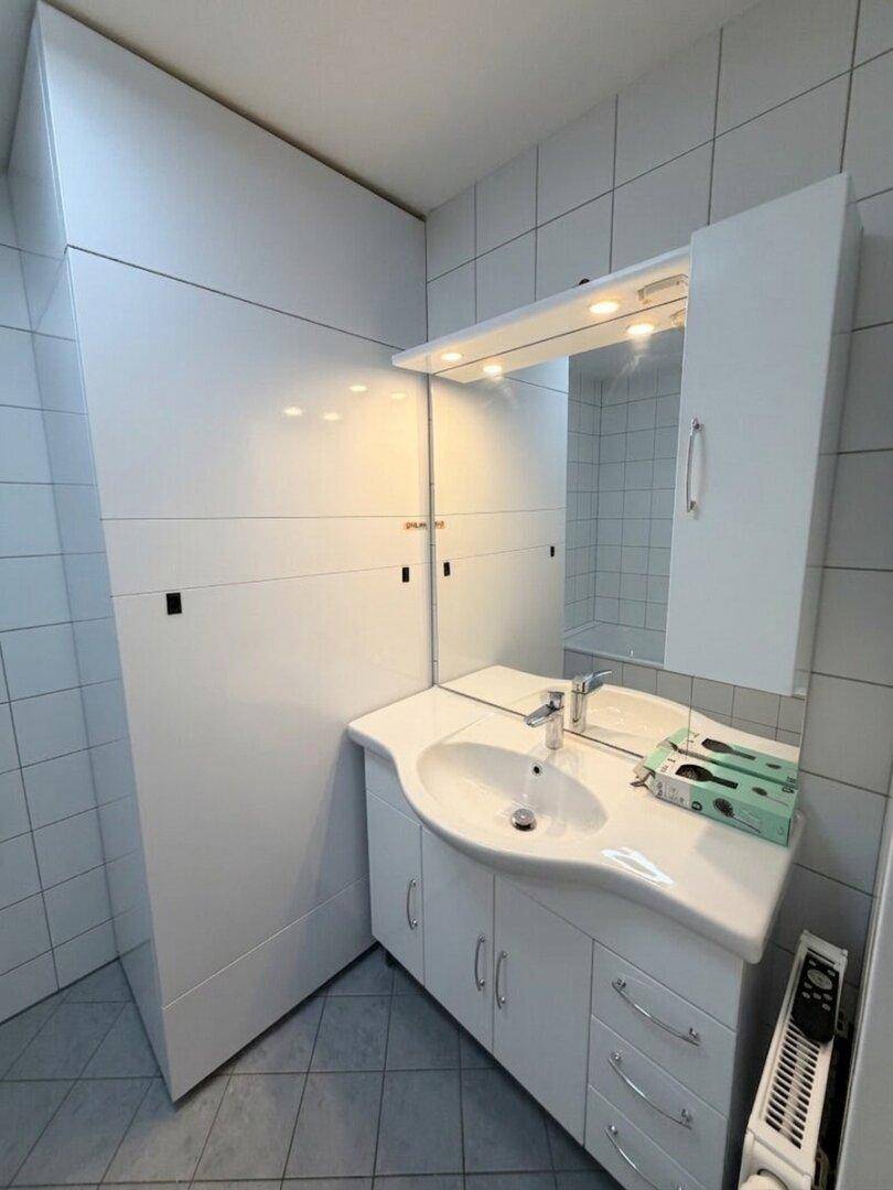Waschbeckenbereich im Badezimmer mit großem Spiegel, Beleuchtung und Stauraum.