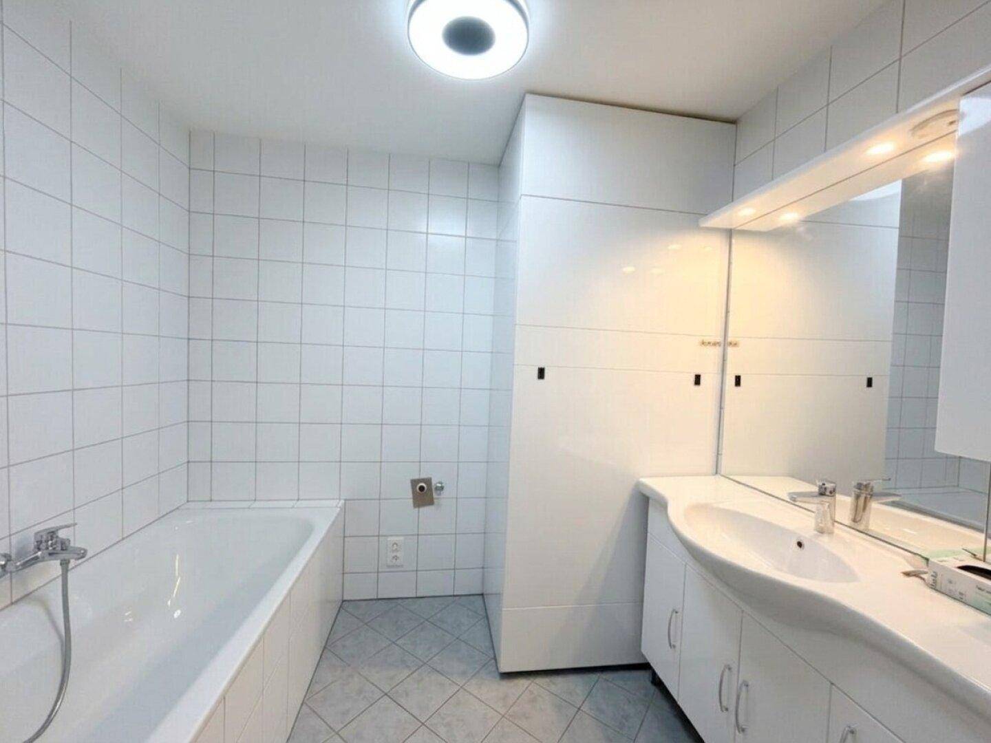 Badezimmer mit Badewanne, Waschbecken mit Unterschrank und großem Spiegel.
