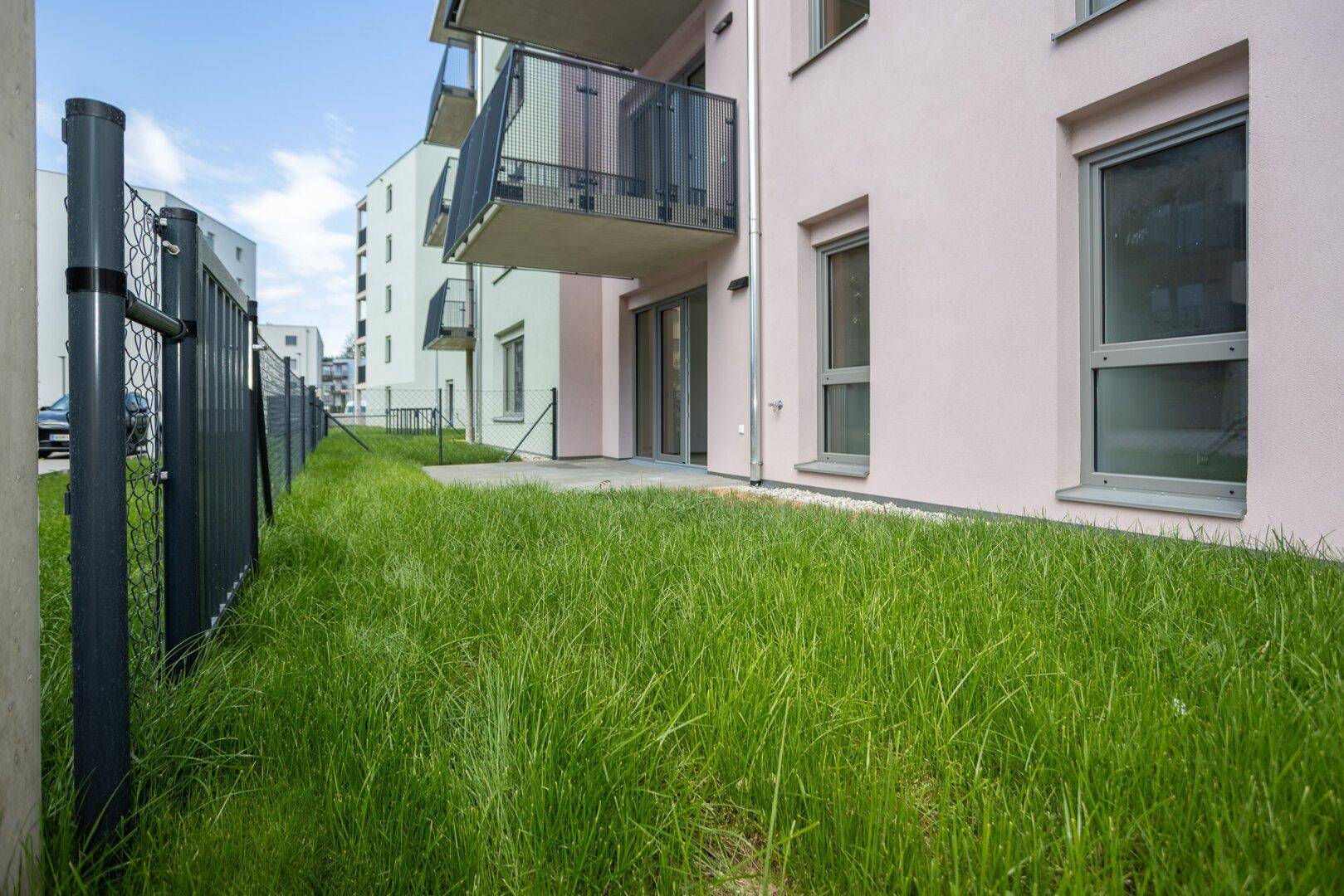 Außenbereich mit Rasenfläche, Terrasse und Balkonen an einem modernen Wohngebäude.