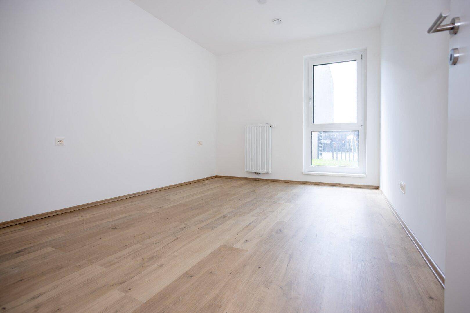 Leeres Schlafzimmer mit hellem Laminatboden und einem Fenster für Tageslicht.