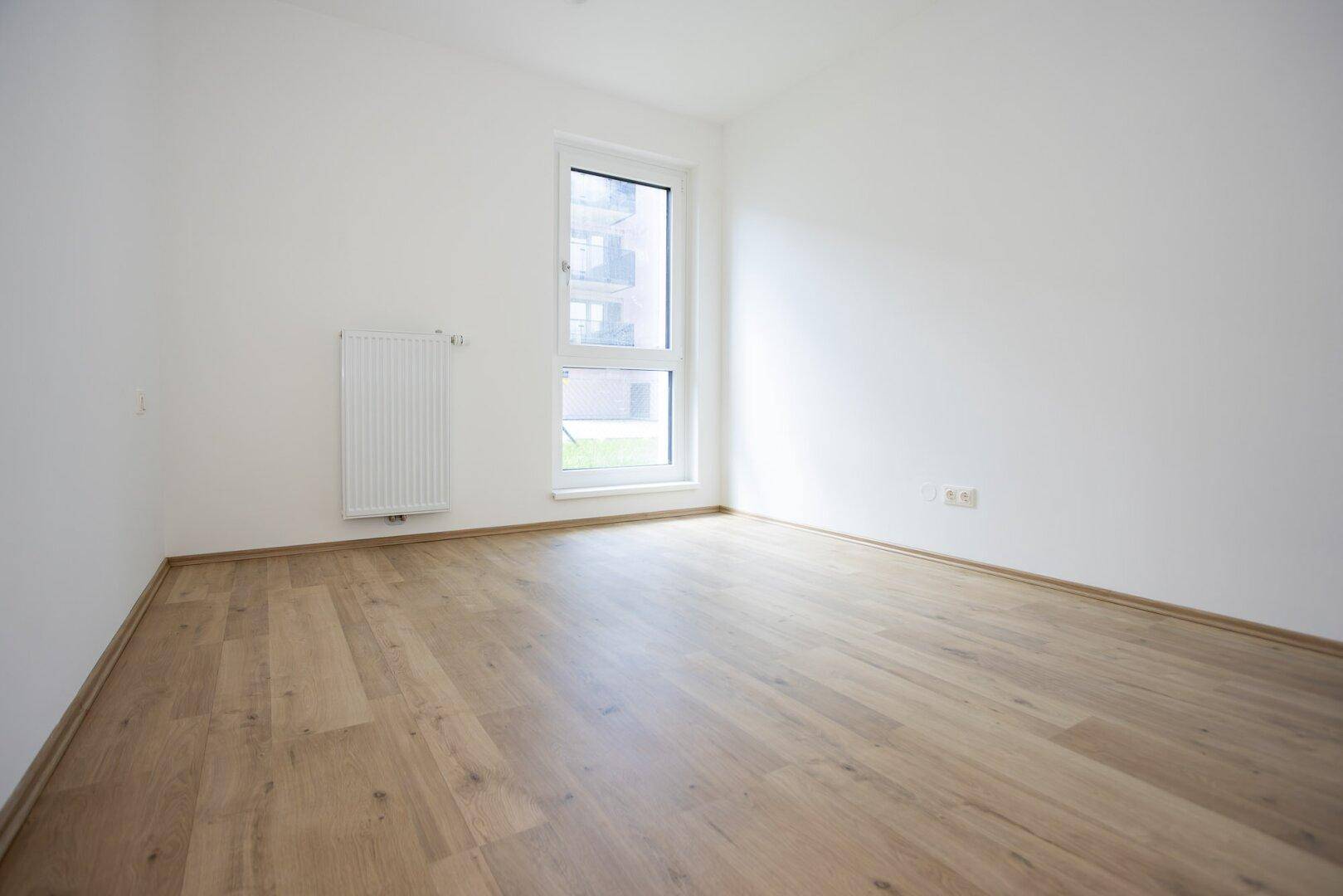 Leeres Schlafzimmer mit hellem Laminatboden und einem Fenster mit Blick nach draußen.