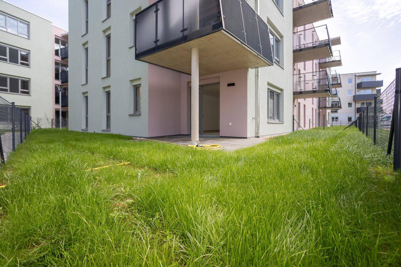 Grüne Rasenfläche vor dem Gebäude mit einer kleinen Terrasse und Balkonen darüber.