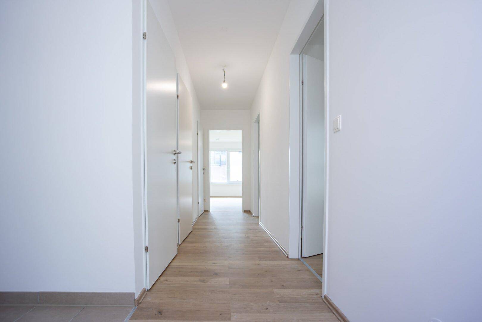 Langer, heller Flur mit Laminatboden und mehreren Türen zu den angrenzenden Räumen.