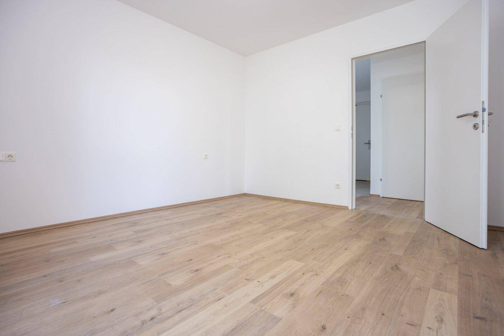 Leeres Zimmer mit hellem Laminatboden und weiß gestrichenen Wänden, ideal als Schlafzimmer.