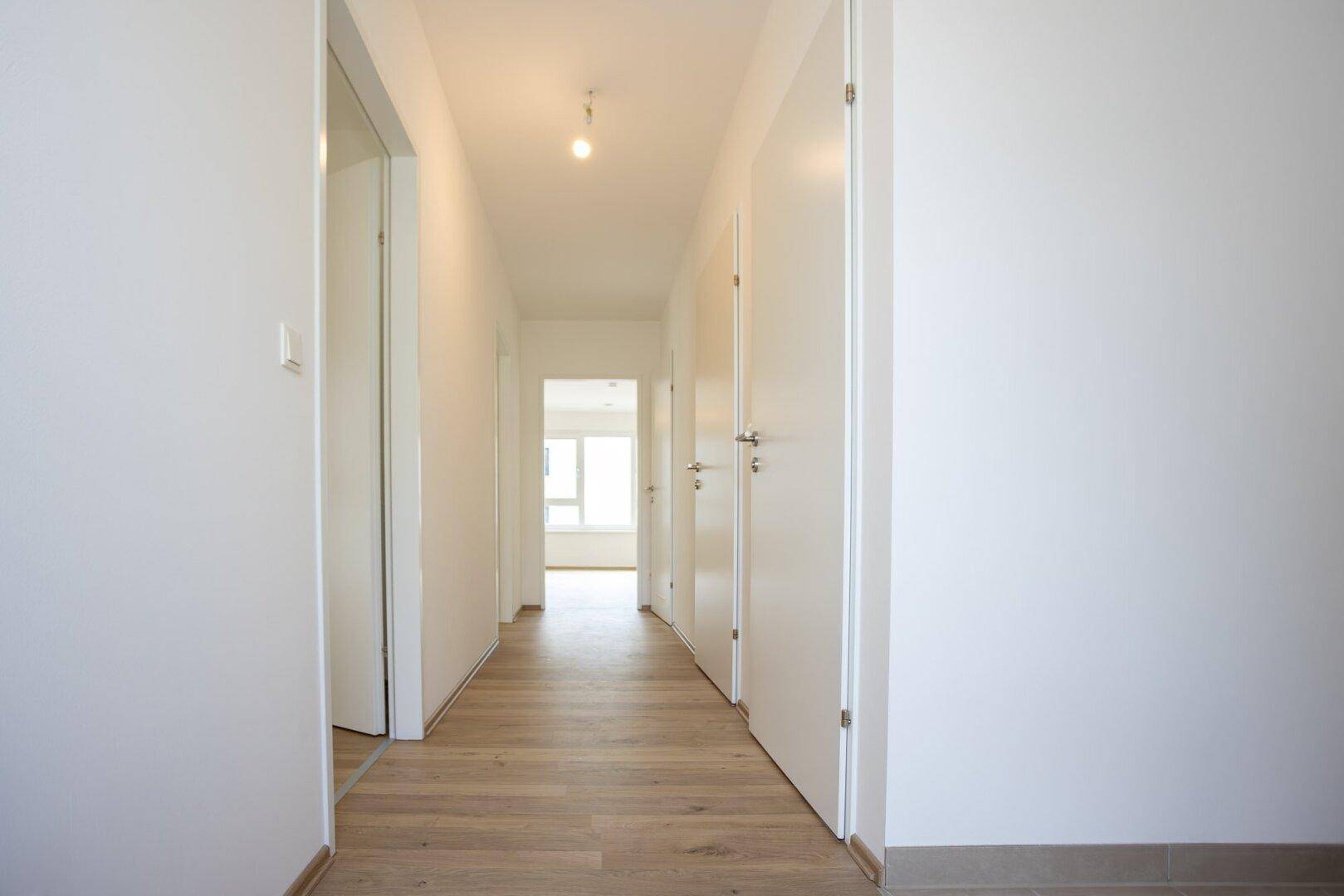Langer, heller Flur mit Laminatboden und mehreren Türen, die zu den angrenzenden Räumen führen.