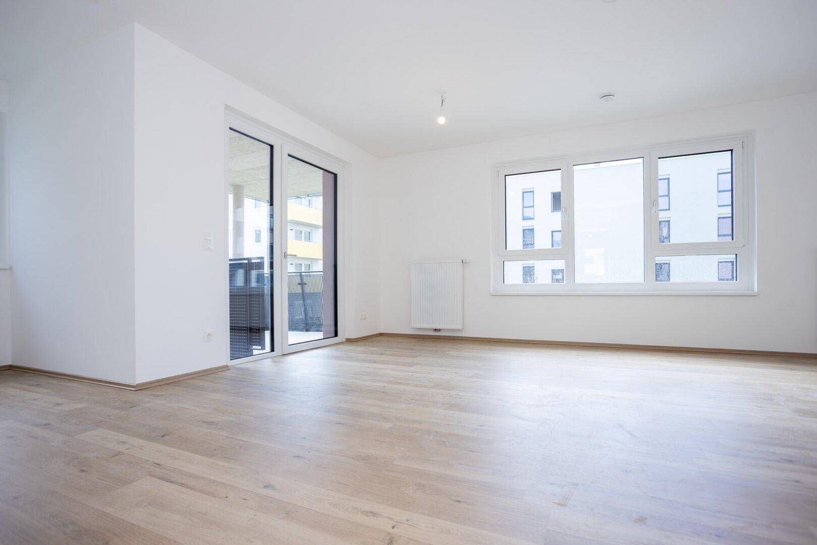 Geräumiger, heller Wohnbereich mit großen Fenstern, Balkontür und modernem Laminatboden.