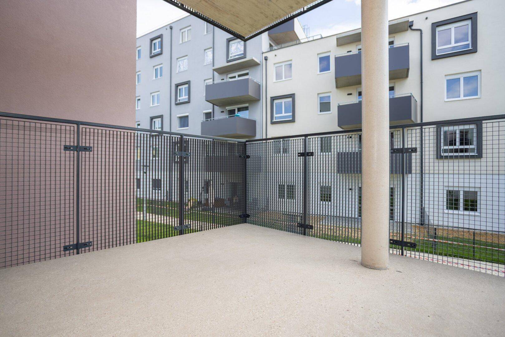 Geräumiger Balkon mit Gittergeländer und Blick auf die umliegenden Wohngebäude und Grünflächen.