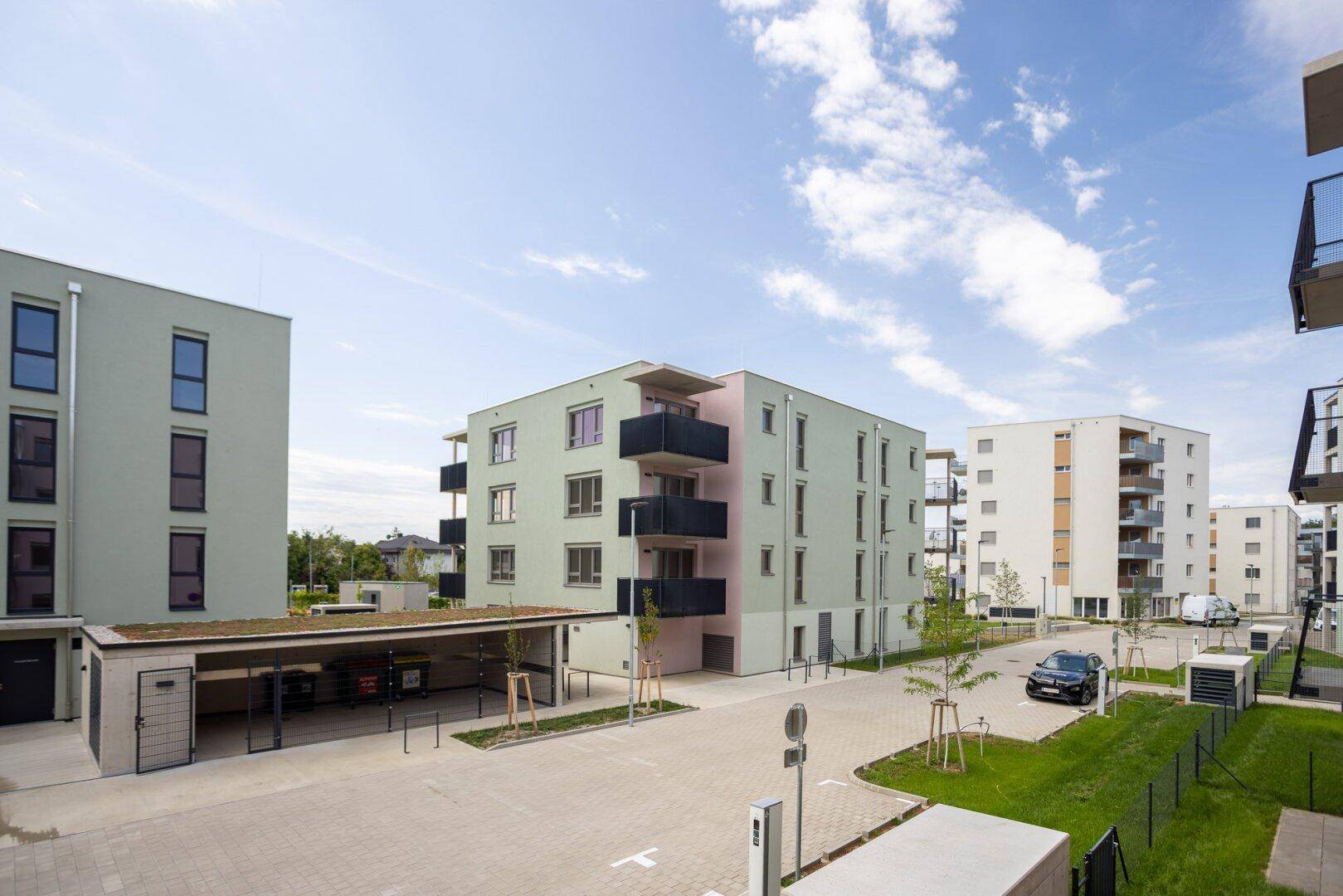 Moderne Wohngebäude mit Balkonen und Carports in einer gepflegten Wohnanlage unter blauem Himmel.