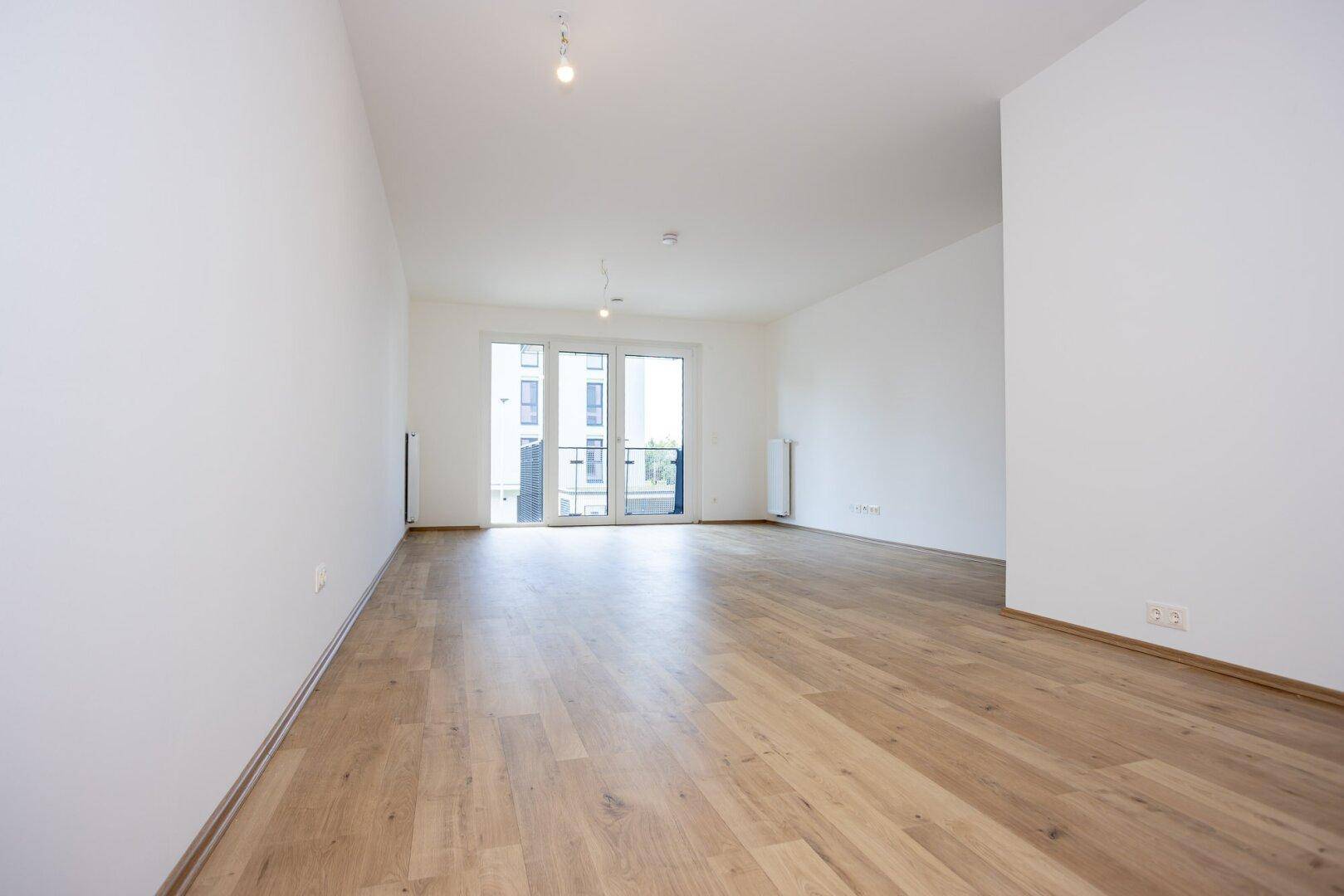Geräumiger, heller Wohnbereich mit Laminatboden und direktem Zugang zu einem Balkon oder einer Terrasse.