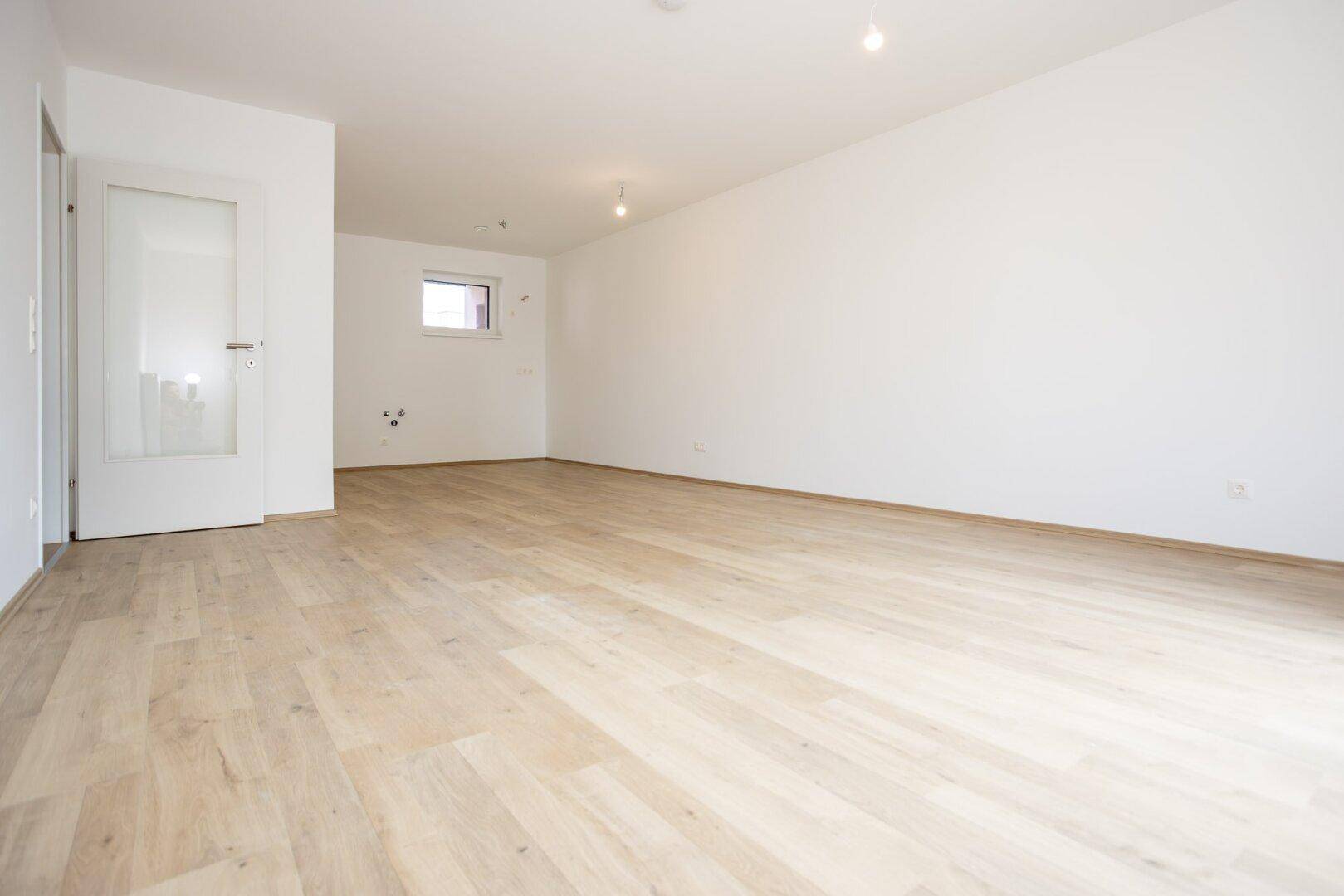 Heller, leerer Wohnraum mit hellem Laminatboden und weiß gestrichenen Wänden, ideal für individuelle Gestaltung.