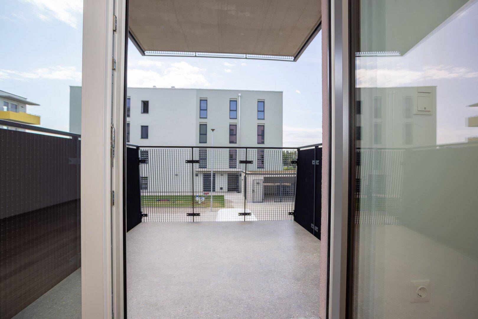Blick vom Innenraum auf den Balkon mit Metallgeländer und die umliegenden modernen Wohngebäude.