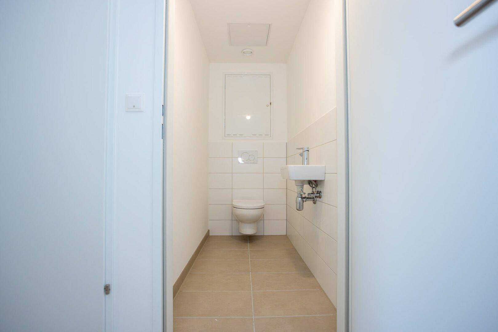 Modernes Gäste-WC mit Wand-WC, kleinem Waschbecken und hellen Fliesen.
