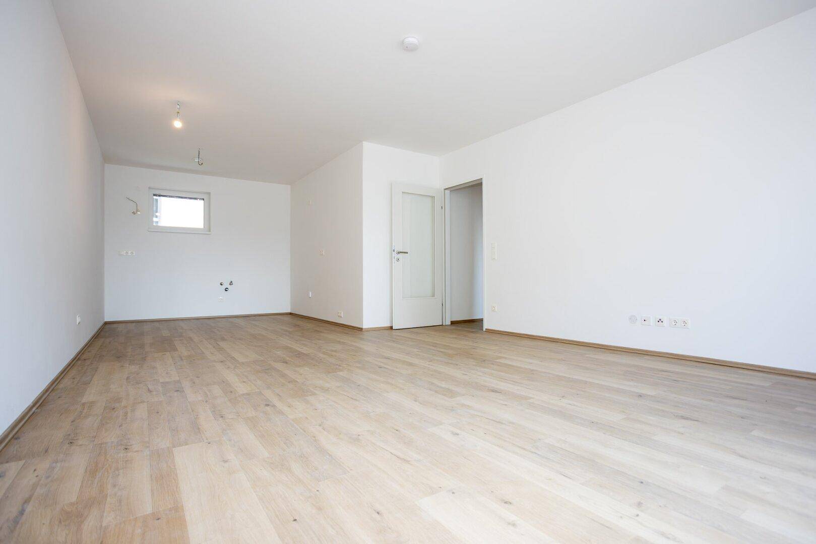 Heller, leerer Wohnraum mit hellem Laminatboden und weißen Wänden, bereit zur individuellen Gestaltung.