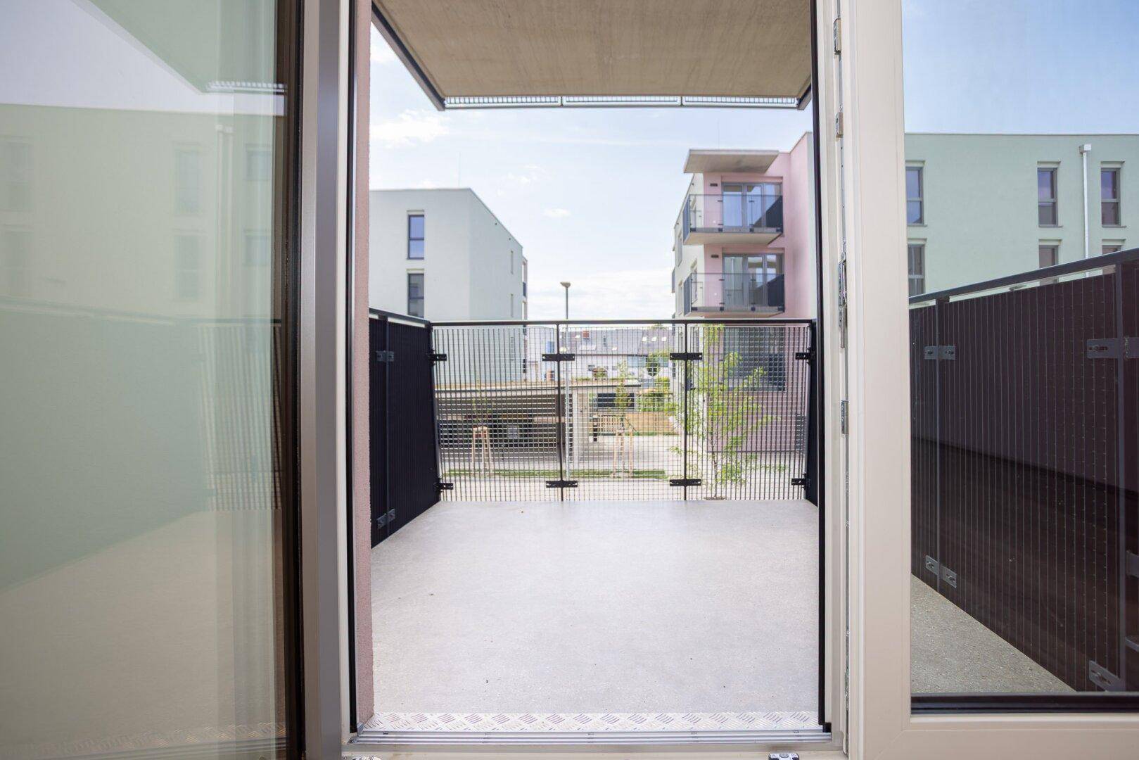 Blick vom Innenraum auf die private Terrasse mit Metallzaun und umliegenden Gebäuden.