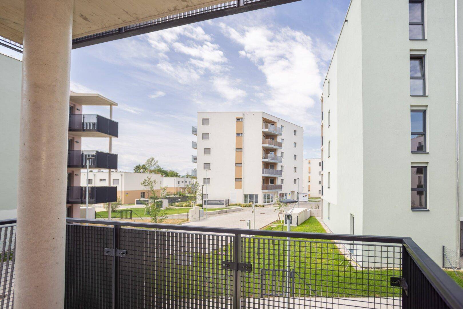 Weitläufiger Blick vom Balkon auf die moderne Wohnanlage mit Grünflächen und weiteren Gebäuden.