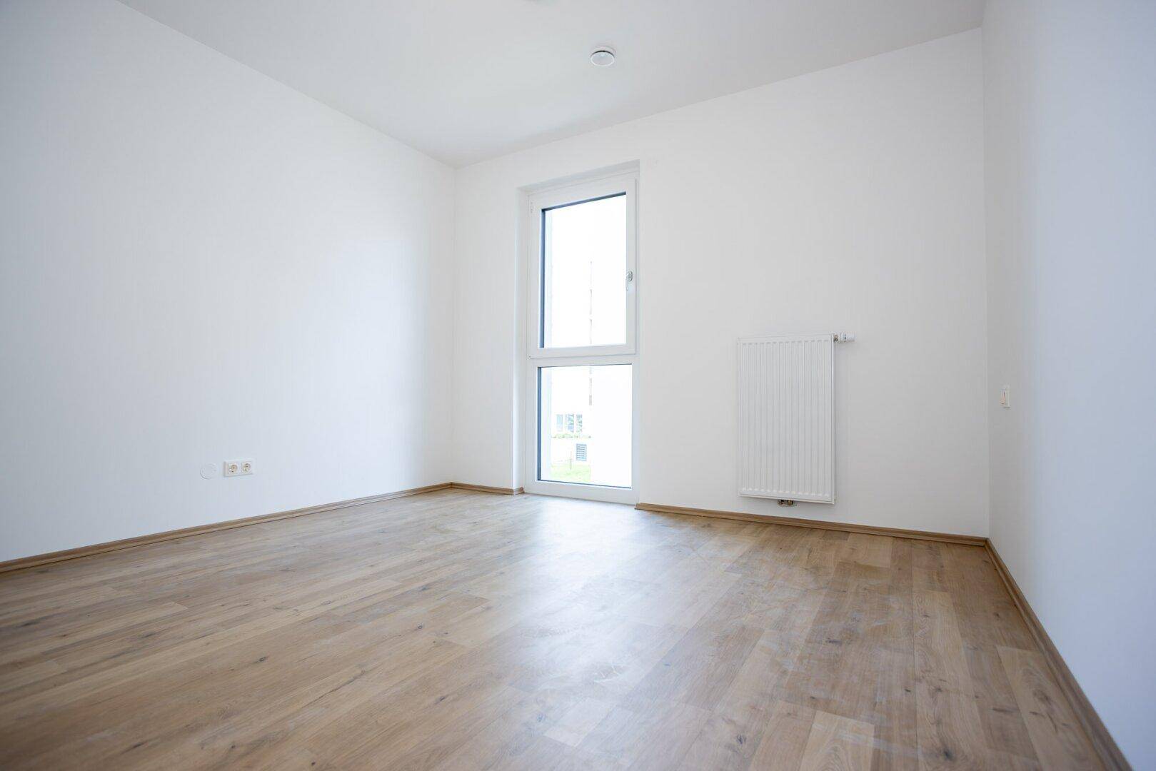 Freundliches Zimmer mit Laminatboden und hohem Fenster, geeignet als Kinder- oder Gästezimmer.