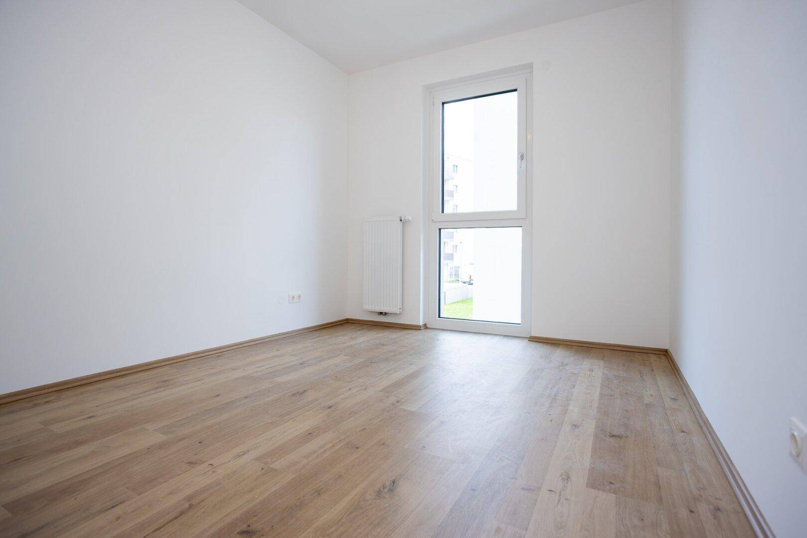 Lichtdurchflutetes Zimmer mit Laminatboden und großem Fenster, ideal für vielfältige Nutzung.