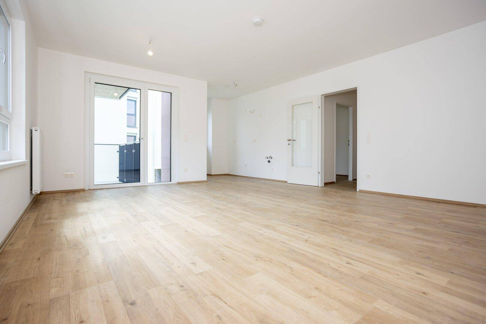 Geräumiger Wohnbereich mit hellem Laminatboden und Schiebetür zum Außenbereich.