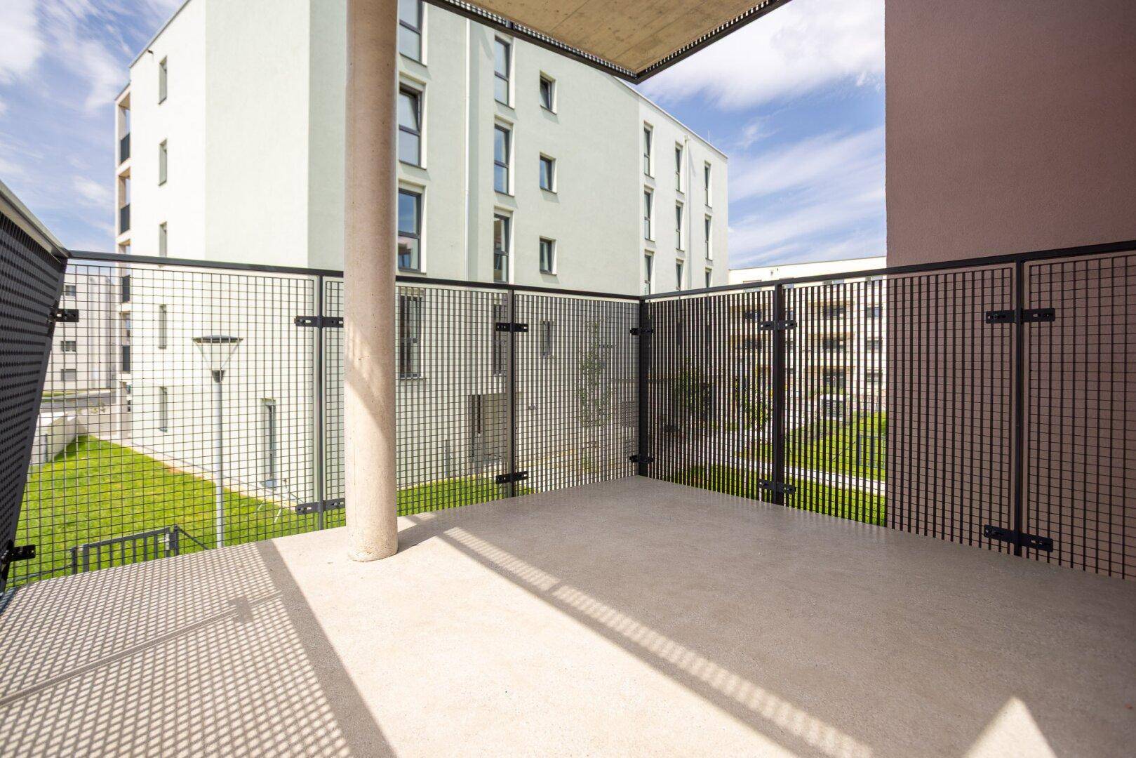 Geräumiger Balkon mit Gittergeländer und Blick auf die umliegenden Neubauten und Grünflächen.