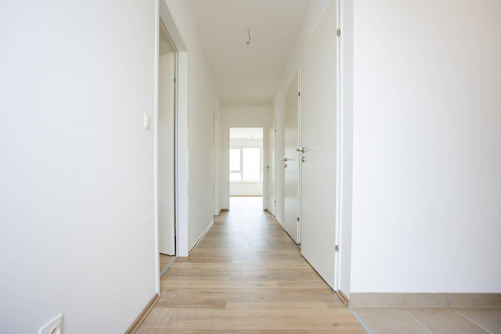 Langer, heller Flur mit Holzboden und Zugang zu mehreren Zimmern der Wohnung.