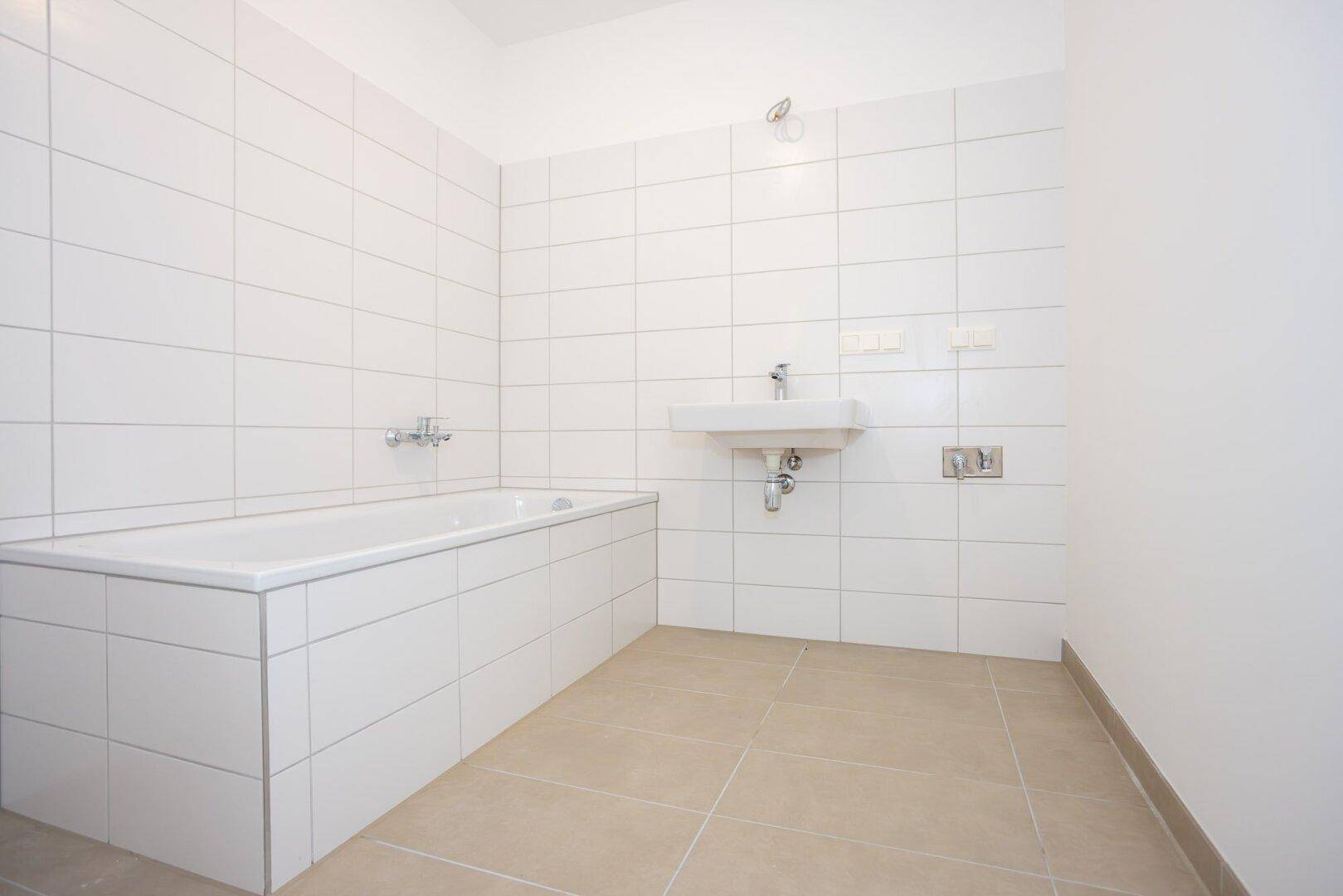 Helles Badezimmer mit Badewanne, Waschbecken und weißen Wandfliesen.