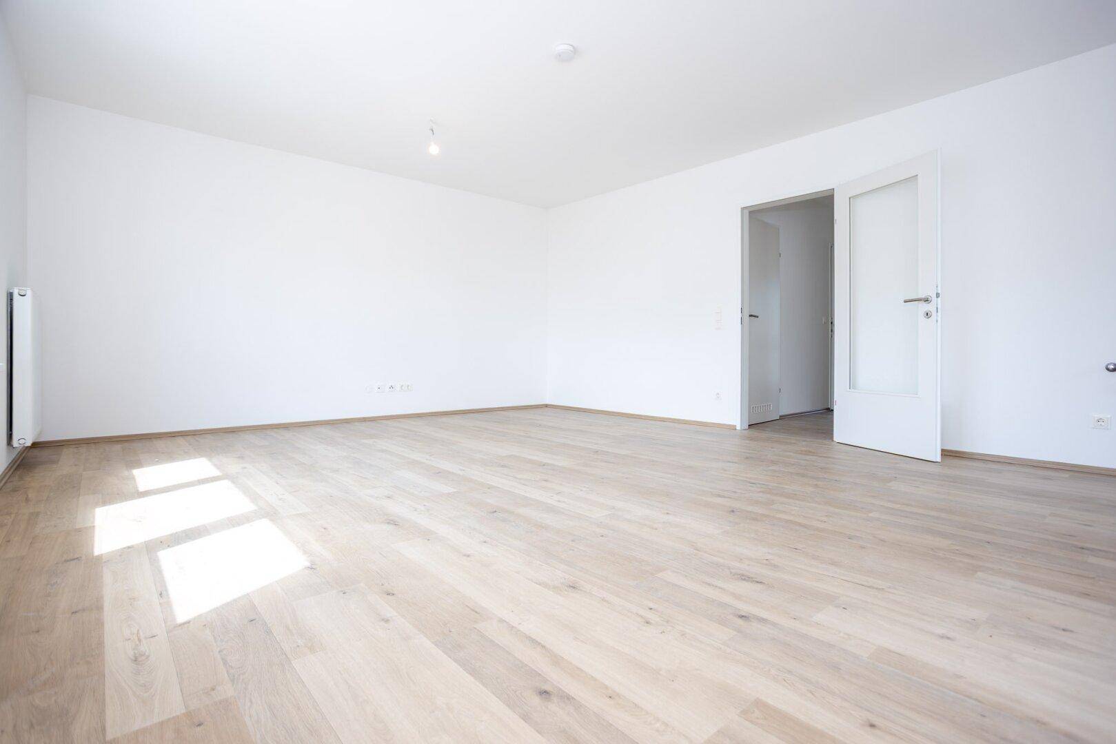 Geräumiger, heller Wohnraum mit Holzboden und zwei Türen, bereit zur individuellen Gestaltung.