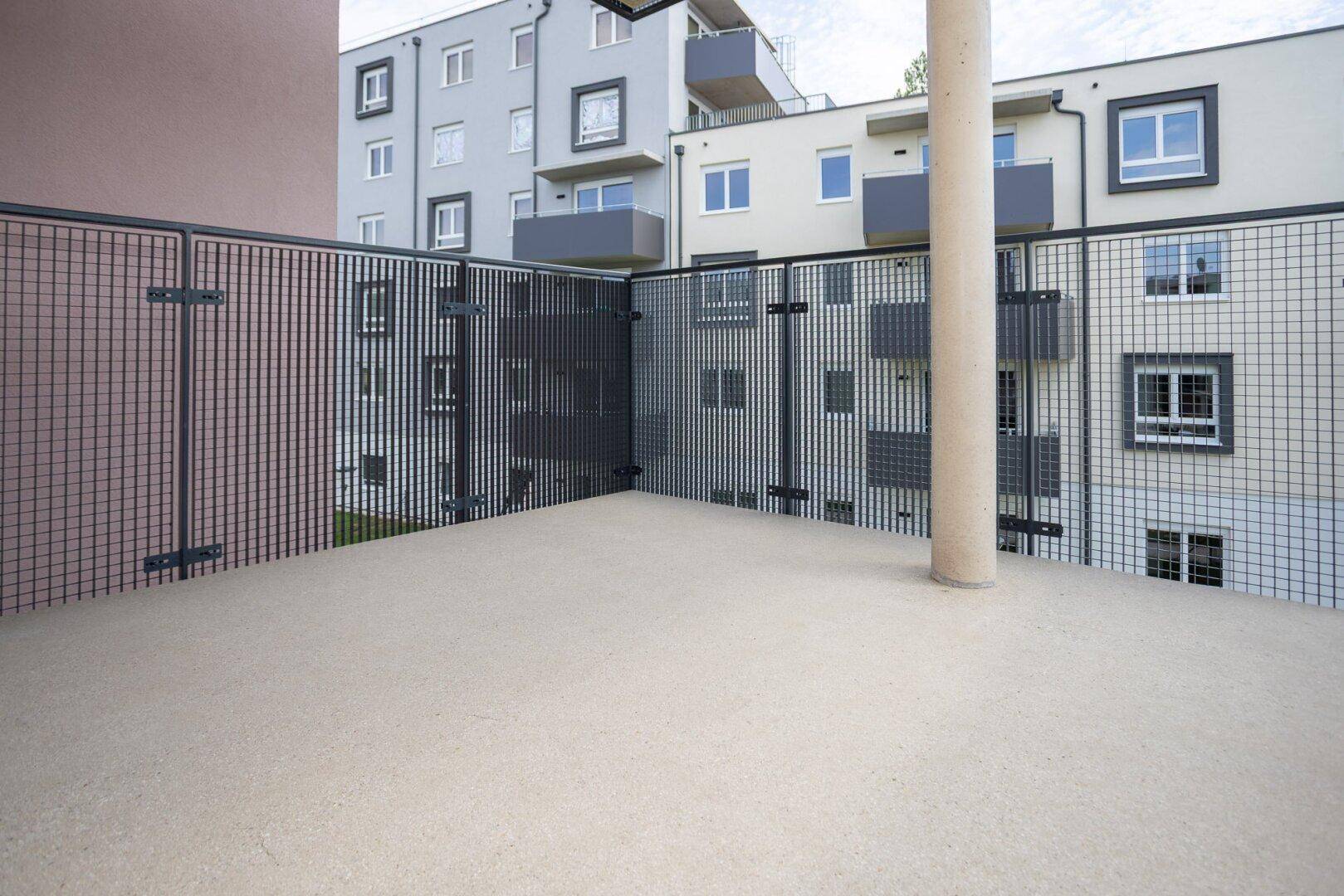 Geräumiger Balkon mit Gittergeländer und Blick auf die umliegenden Gebäude der Wohnanlage.