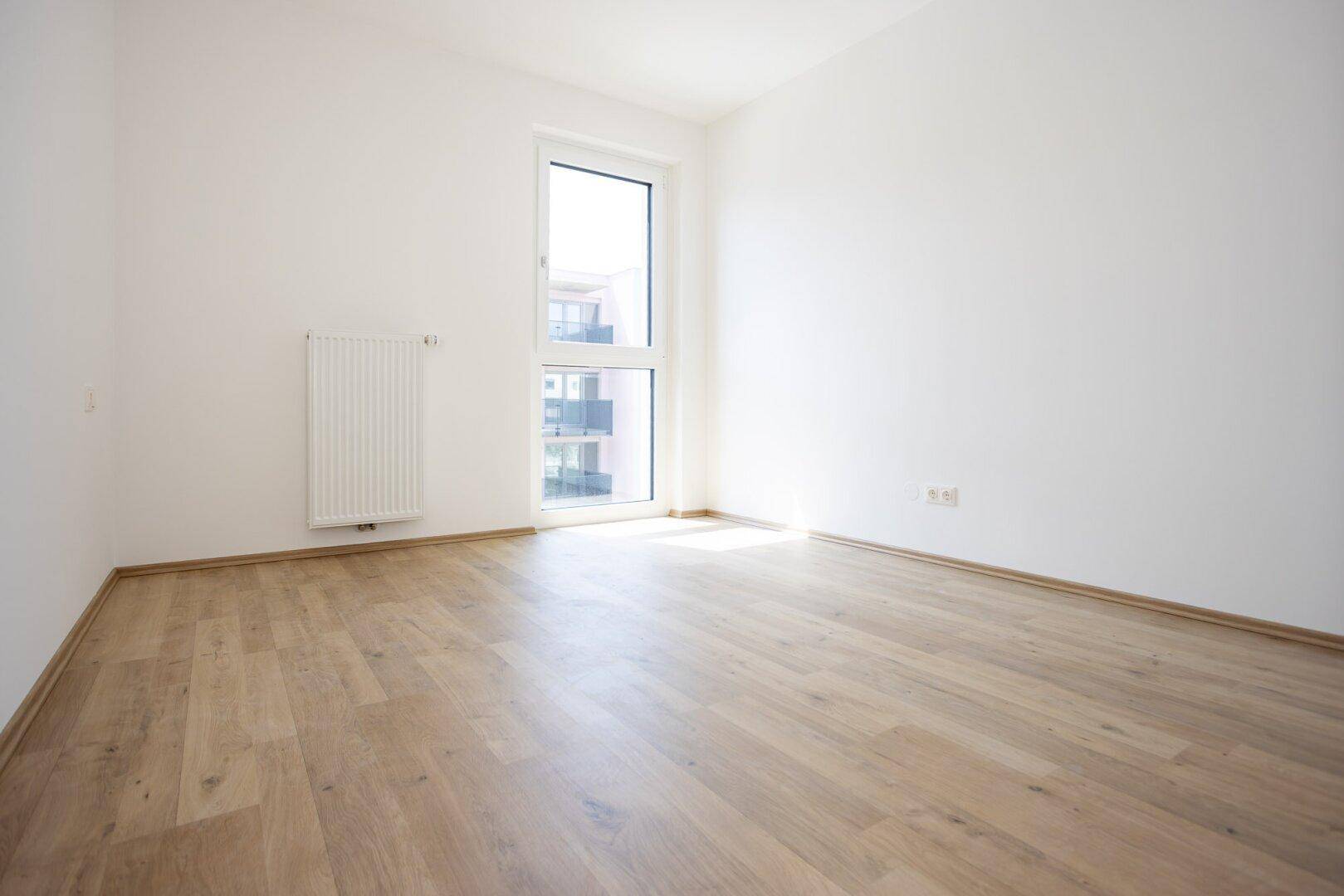 Lichtdurchflutetes Schlafzimmer mit hellem Laminatboden und großem Fenster mit Blick nach draußen.