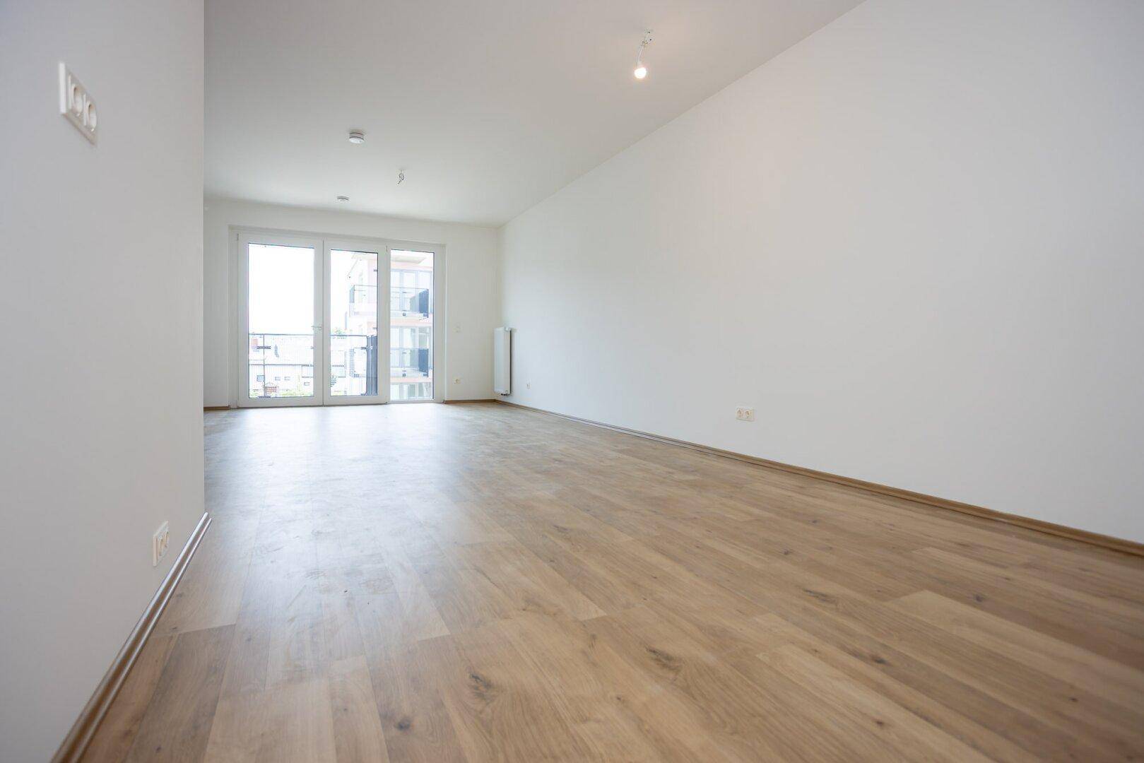 Geräumiger Wohnbereich mit hellem Laminatboden und großen Balkontüren für viel Tageslicht.