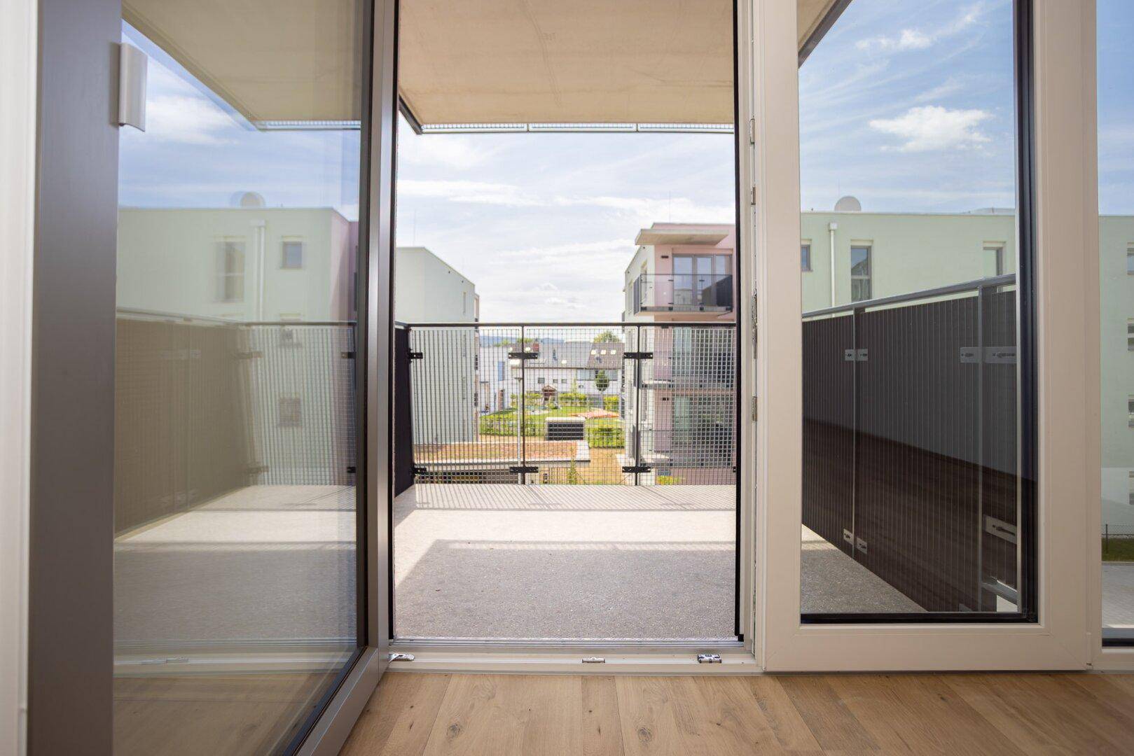 Blick vom Innenraum durch große Glasschiebetüren auf den modernen Balkon und die Umgebung.