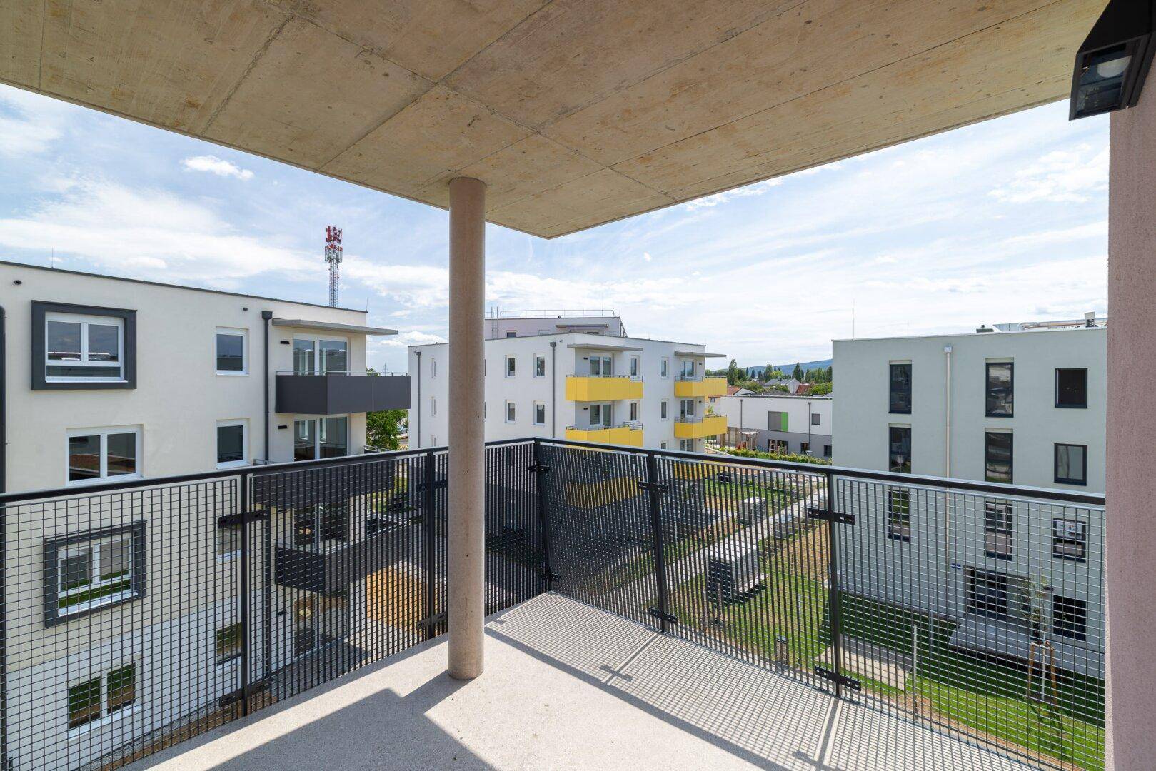 Balkon mit Metallgeländer und Ausblick auf die moderne Wohnsiedlung mit weiteren Gebäuden.