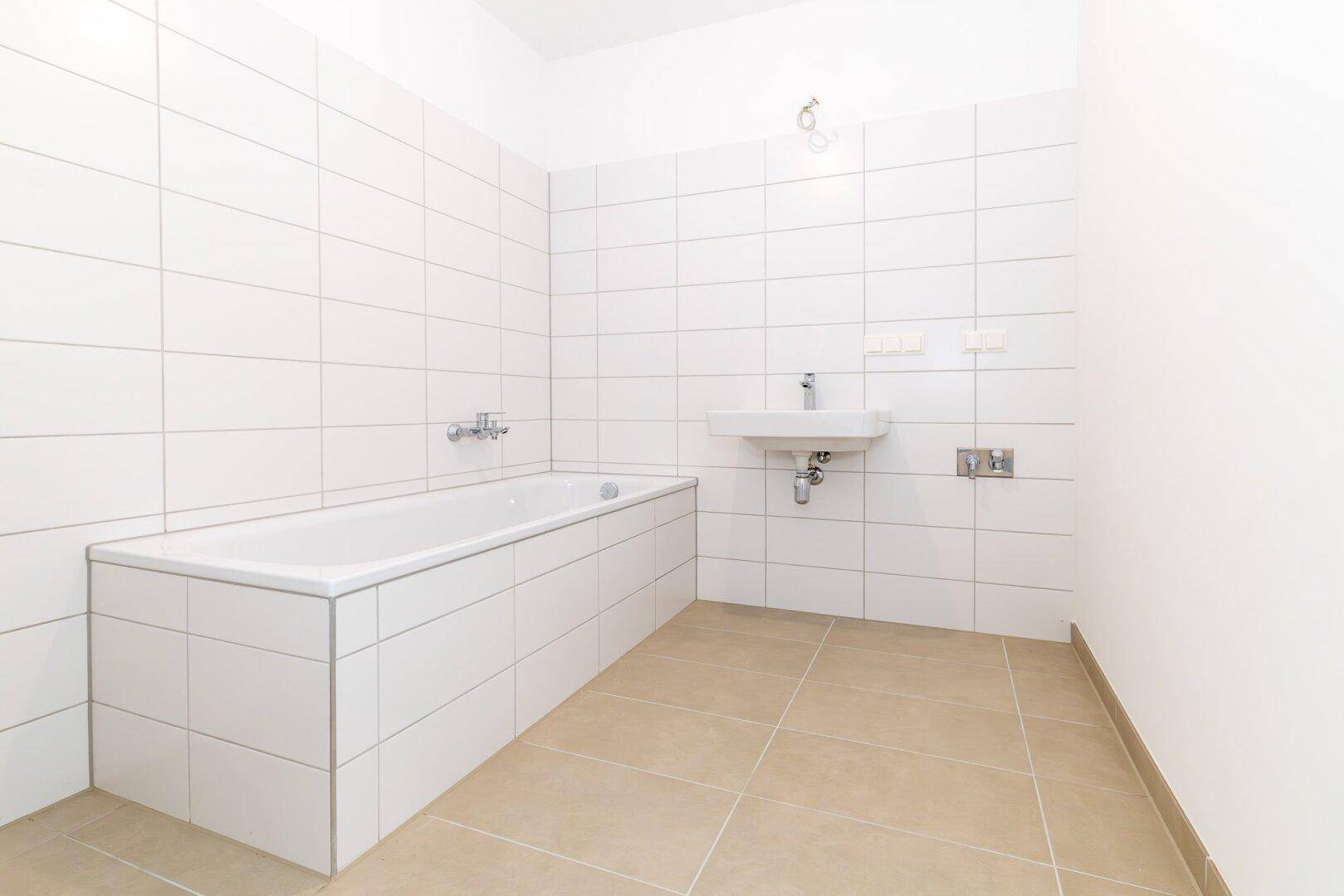 Helles Badezimmer mit Badewanne, Waschbecken und weißen Wandfliesen, bereit zur Nutzung.