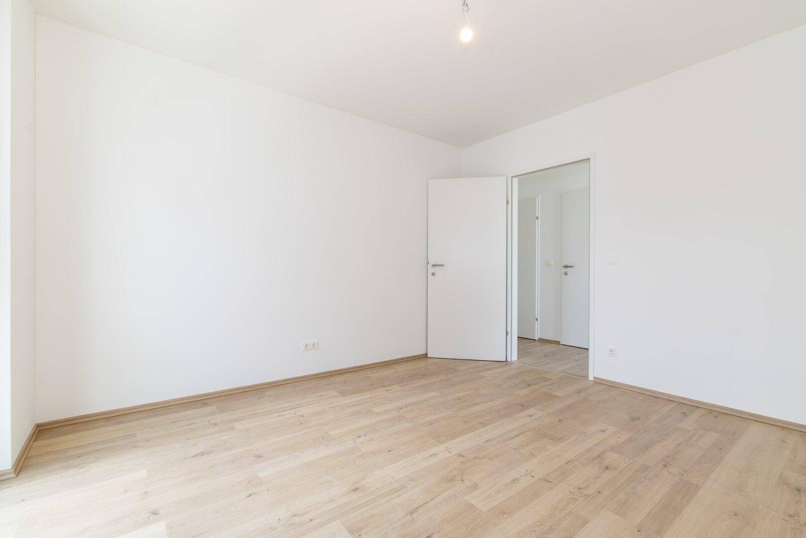 Leeres Zimmer mit hellem Laminatboden und weißen Wänden, bereit für individuelle Gestaltung.