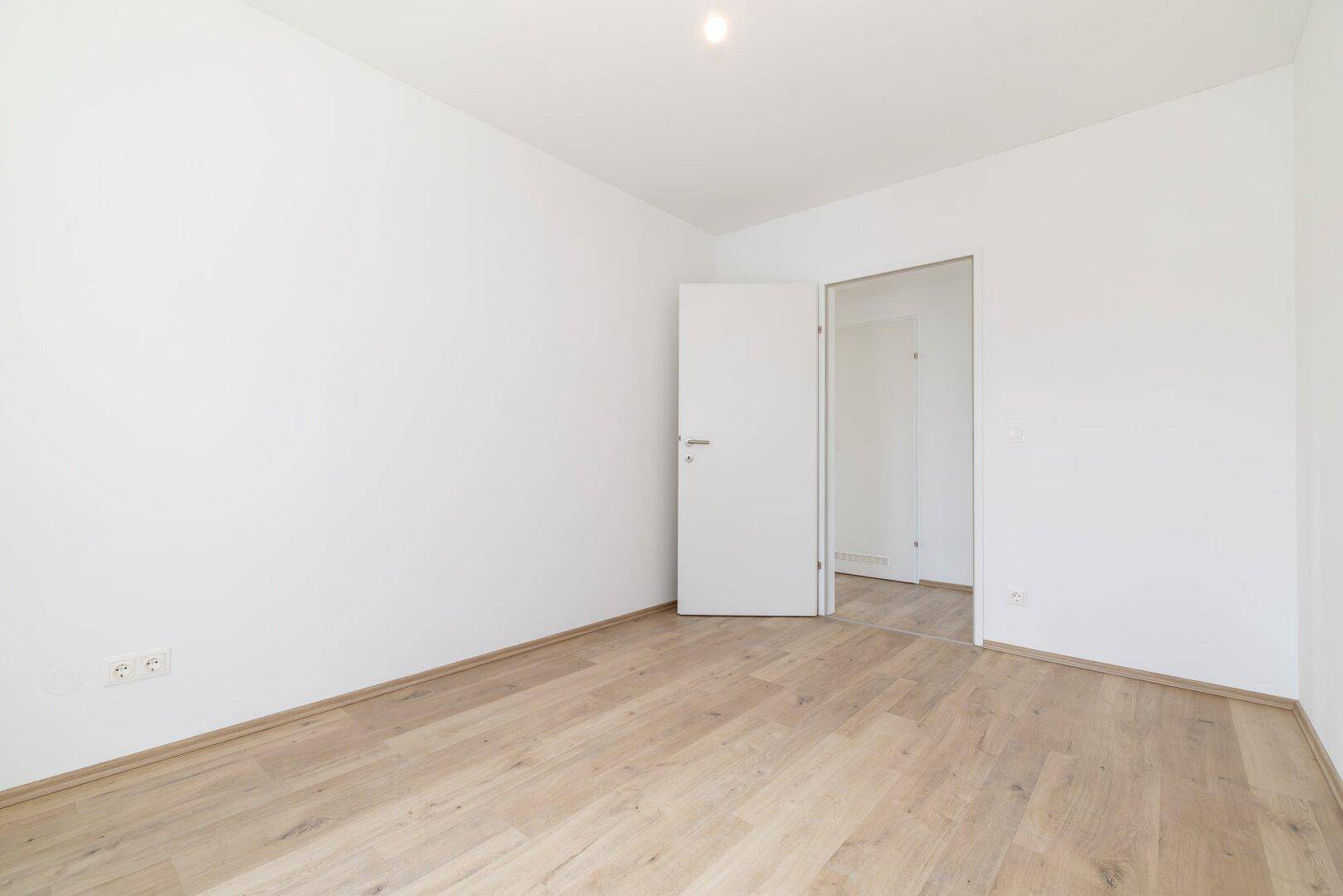 Leeres Zimmer mit Laminatboden und weißen Wänden, bietet flexible Nutzungsmöglichkeiten.